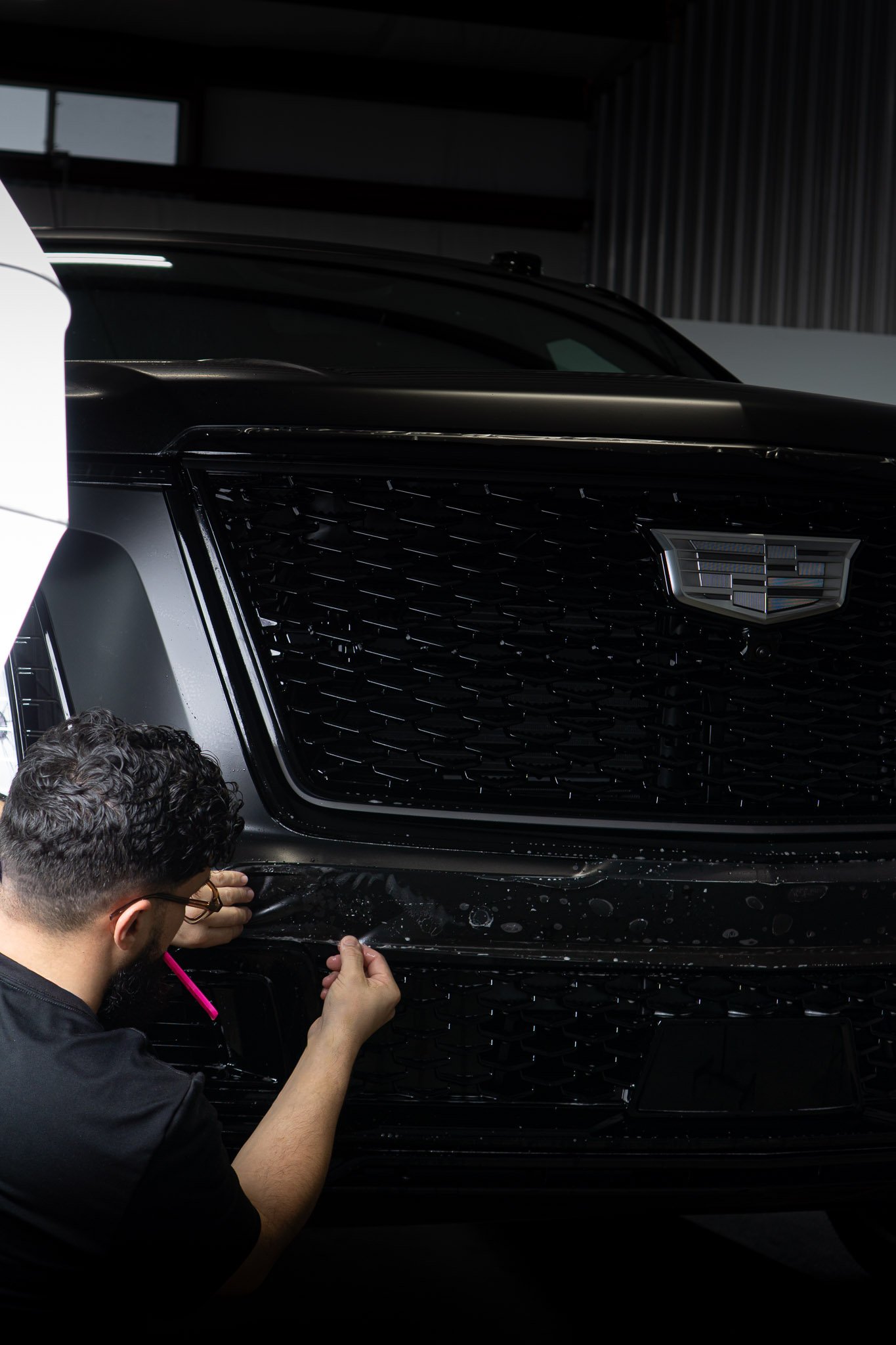 EIGHTYNINE VWS technician installing paint protection film on the front grille of a black Cadillac Escalade for maximum road-debris protection in Little Elm, TX