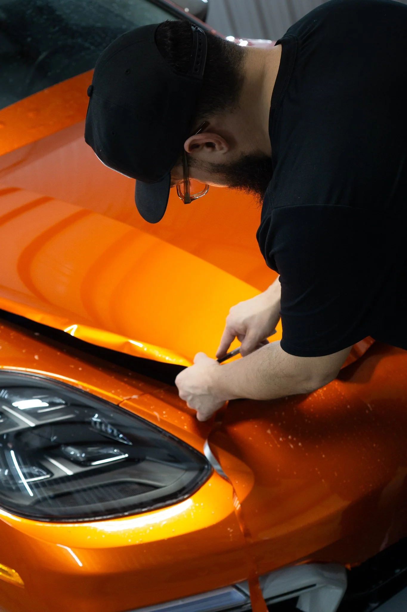 Technician hand-applying orange color change paint protection film to a sports car hood and headlight - EIGHTYNINE VWS color PPF wrap installation in Little Elm, TX