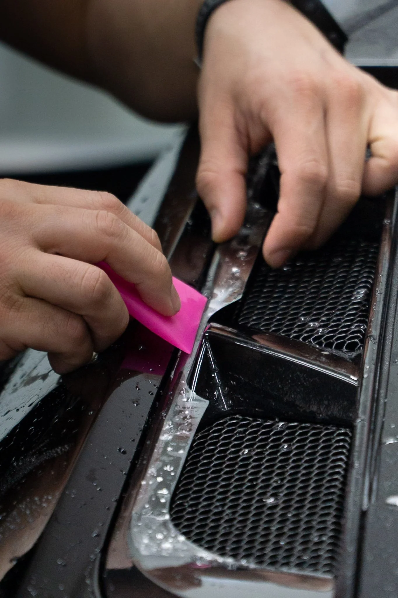 Technician hand-installing paint protection film onto a vehicle's front grille with a squeegee tool - EIGHTYNINE VWS PPF installation process in Little Elm, TX