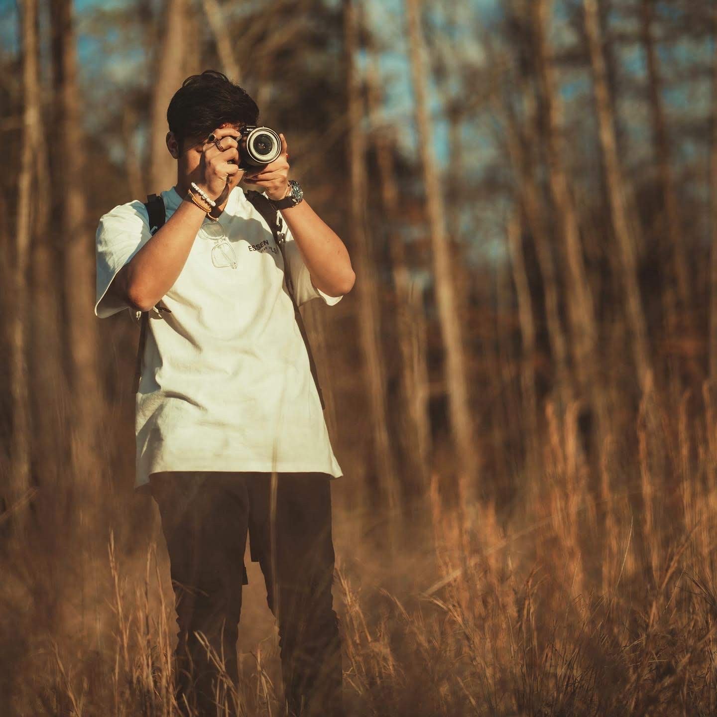 Person taking a photo in a forest standing among tall grass.