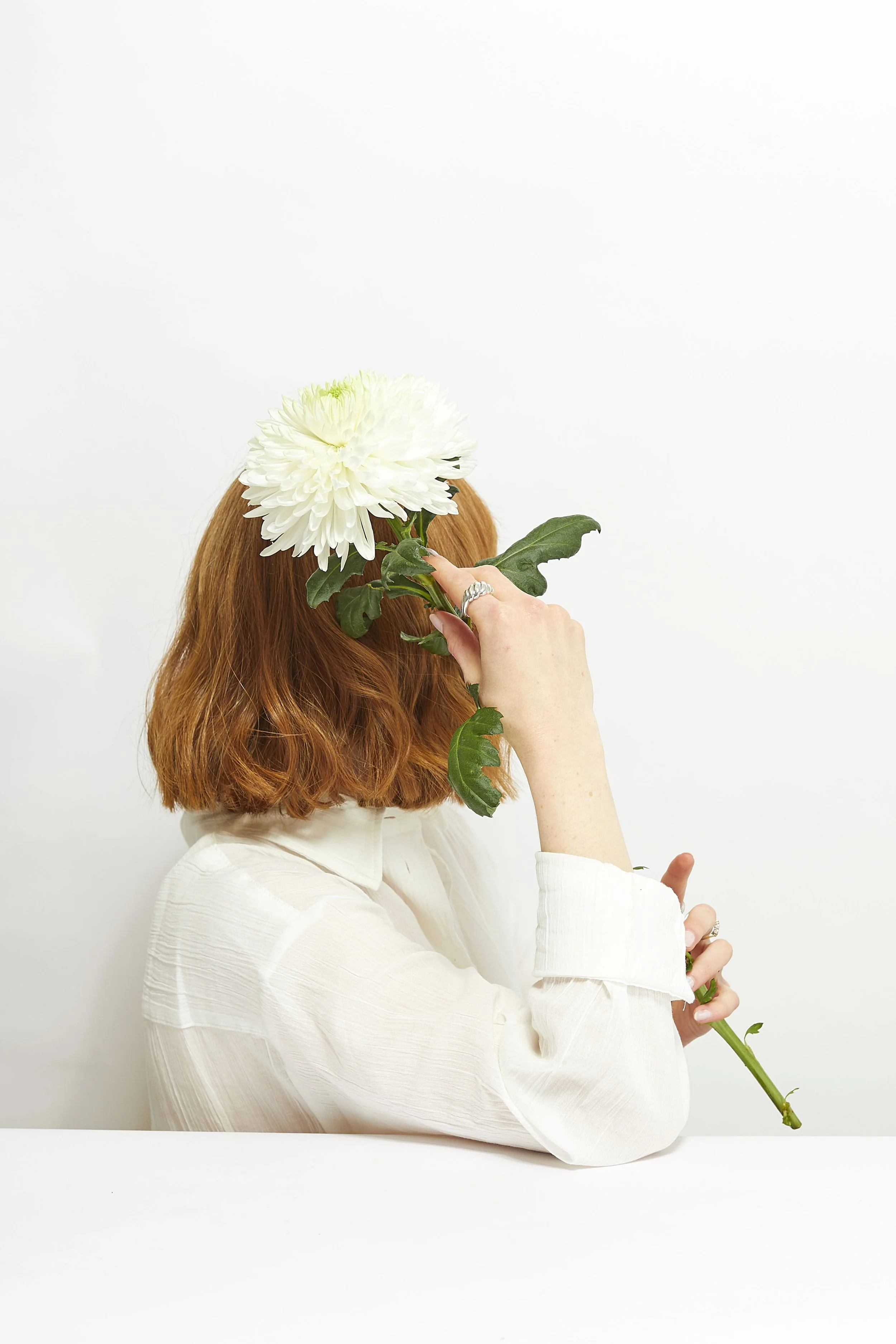 Self portrait studio photography, with a soft commercial aesthetic. Soft lighting, white background and white shirt styling editorial photo shoot. Posing with flowers, white pink and yellow colours. 