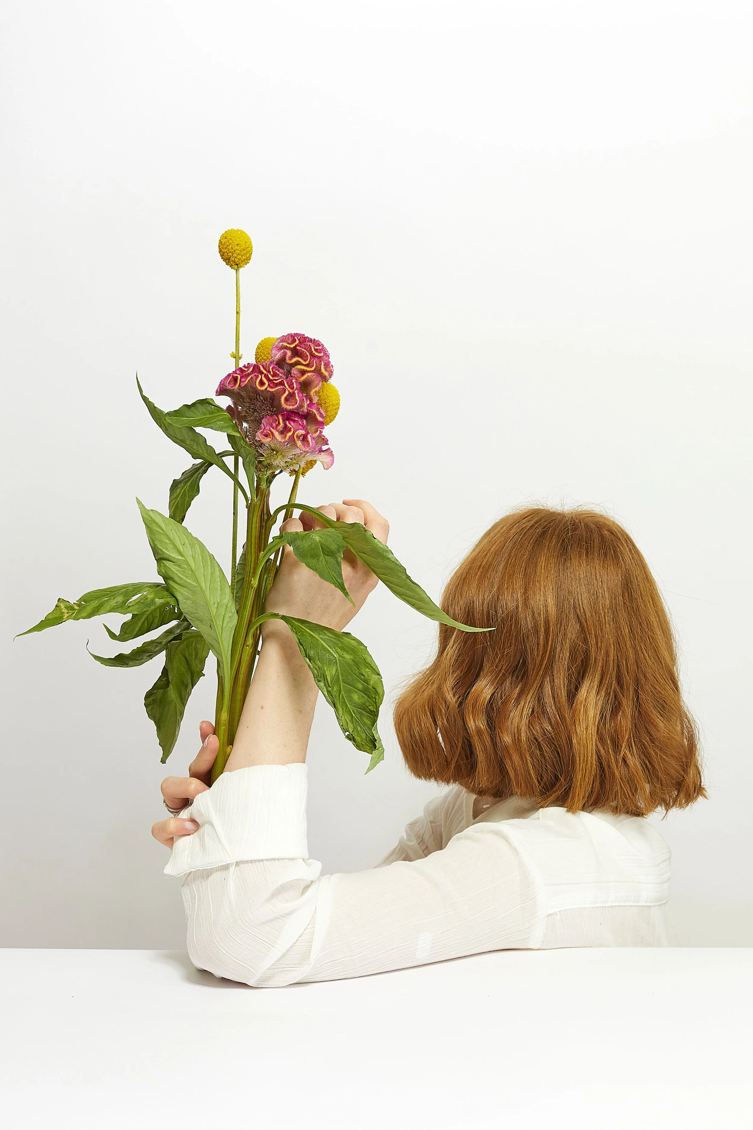 Self portrait studio photography, with a soft commercial aesthetic. Soft lighting, white background and white shirt styling editorial photo shoot. Posing with flowers, white pink and yellow colours.