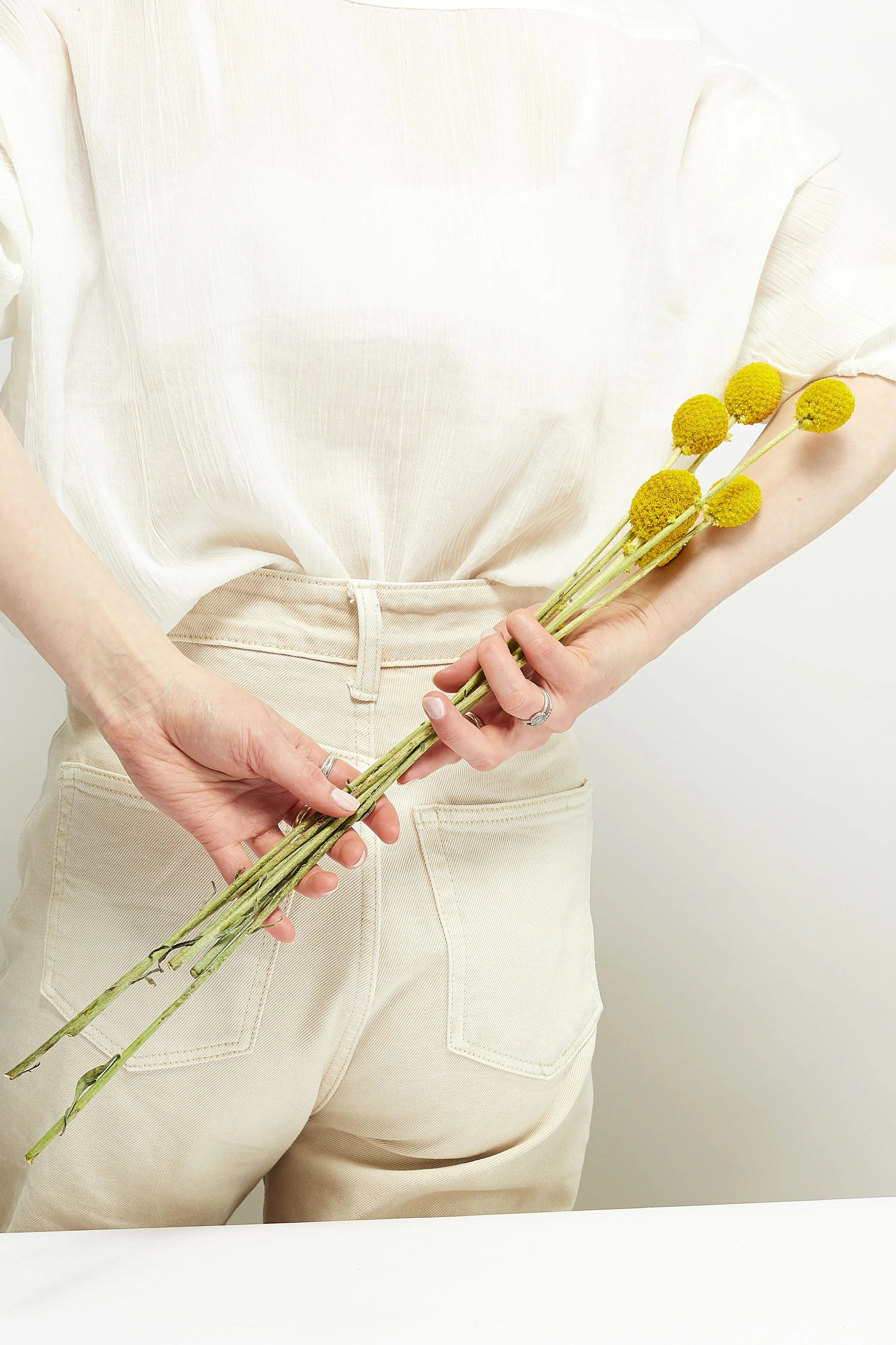 Self portrait studio photography, with a soft commercial aesthetic. Soft lighting, white background and white shirt styling editorial photo shoot. Posing with flowers behind my back, white pink and yellow colours.