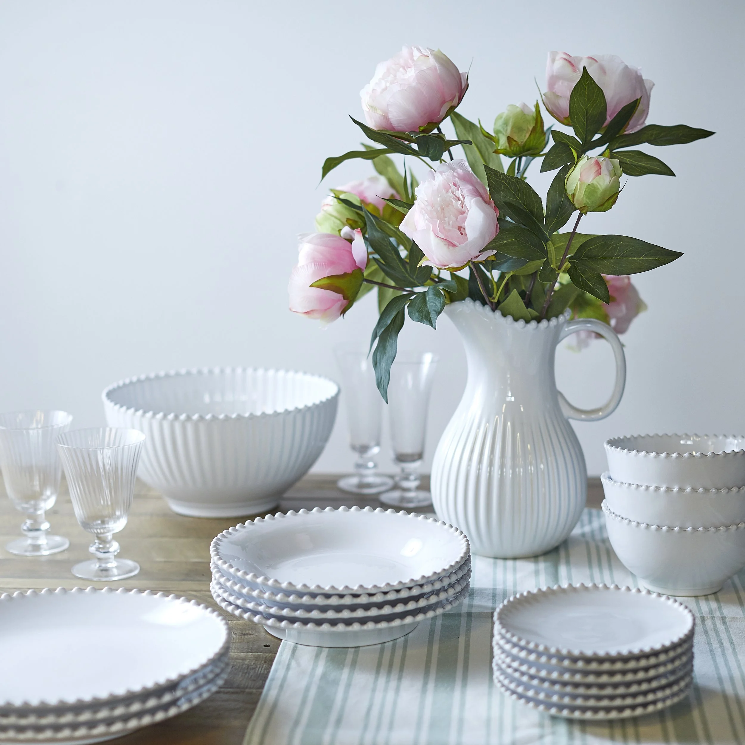 Still life photograph of crockery set and table wear stacked on a wooden table. Photographed in a studio with soft bright studio lighting, creating bright highlights and soft shadows and a shallow depth of field brining sharp focus to the middle and 