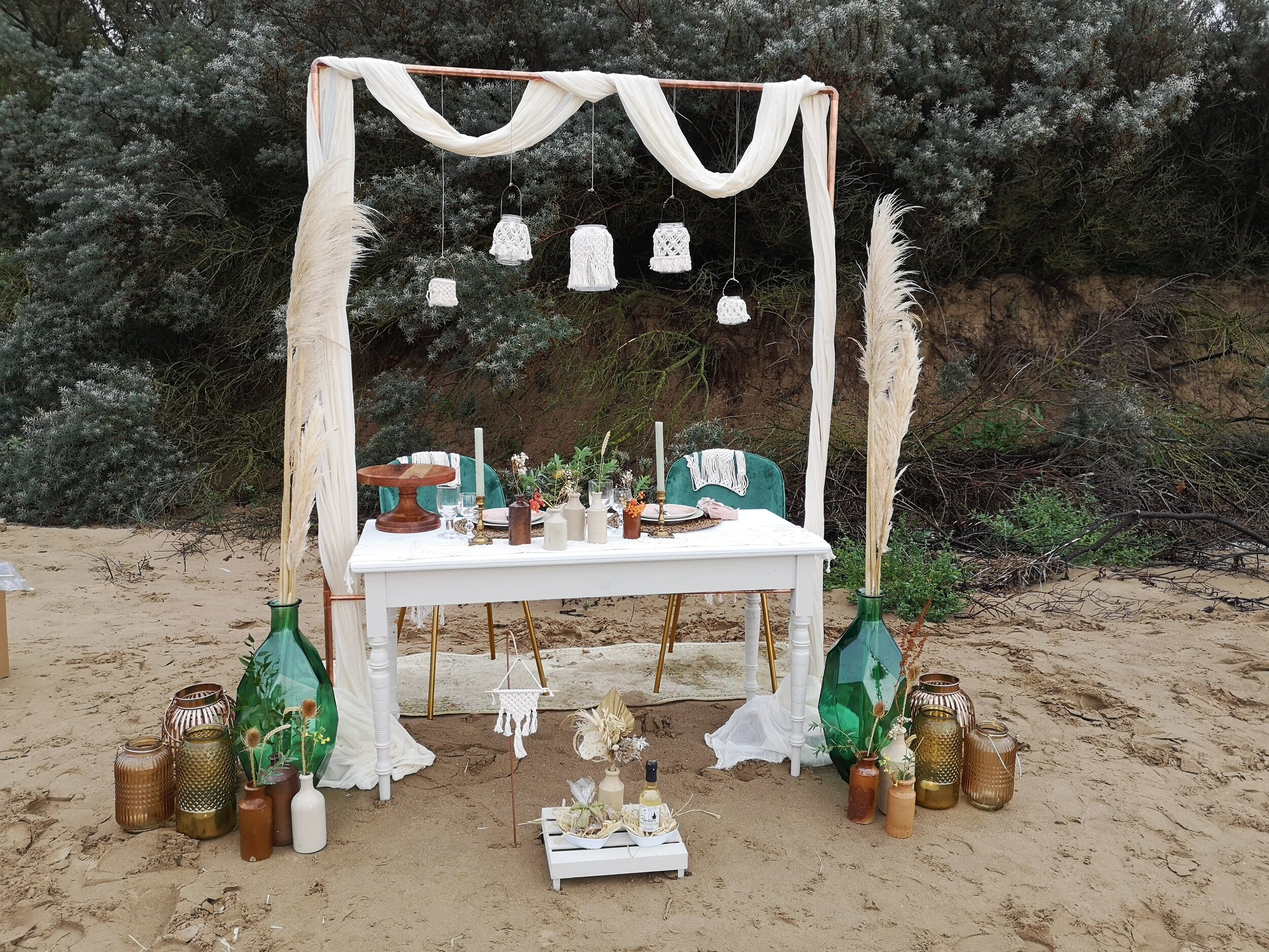 Copper arch holds macrame candle jars over elopement style beach wedding