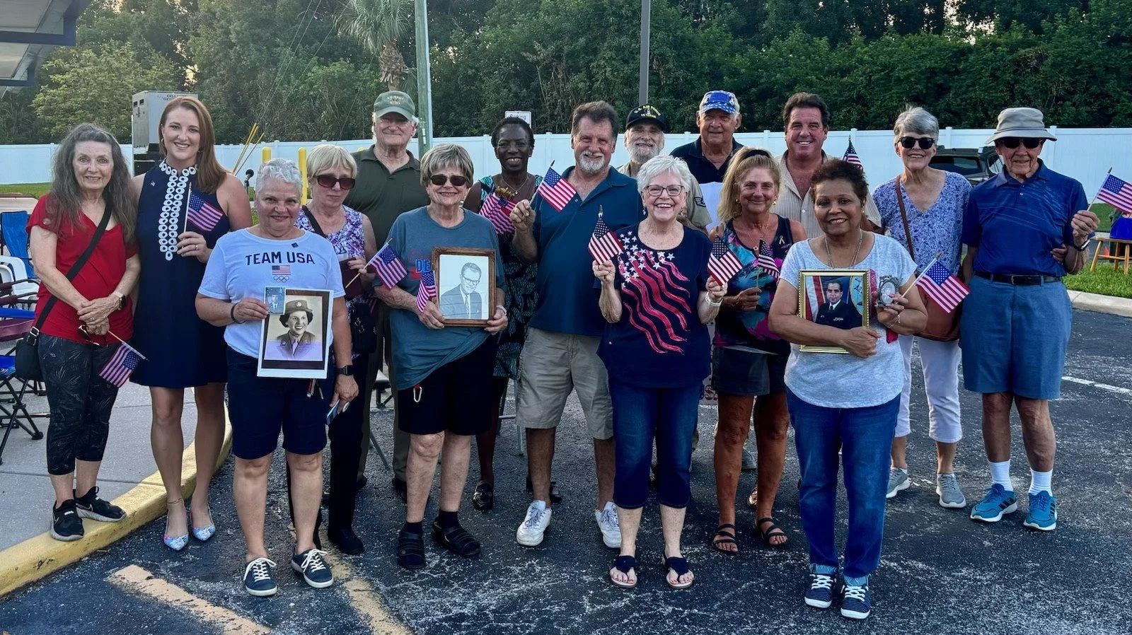 A group of people gathered outdoors holding American flags and framed photos of loved ones, celebrating a patriotic event.