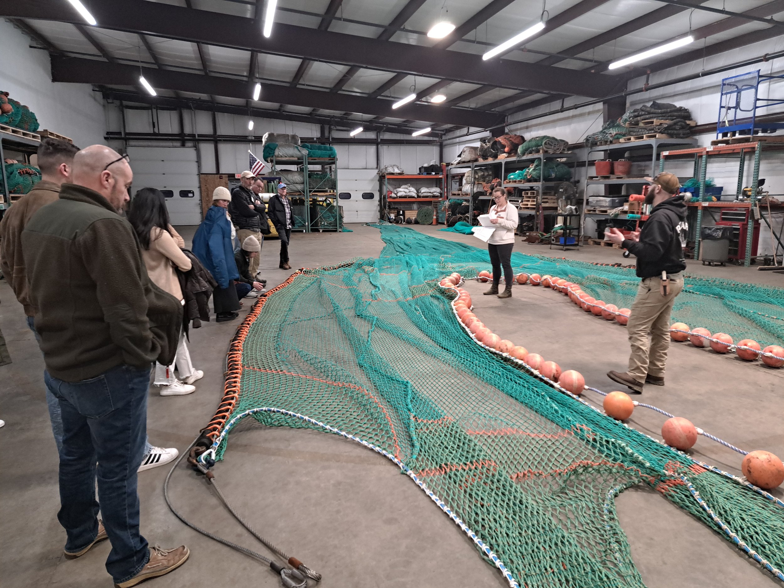 Workshop participants standing around a large green fishing net on the floor in a warehouse