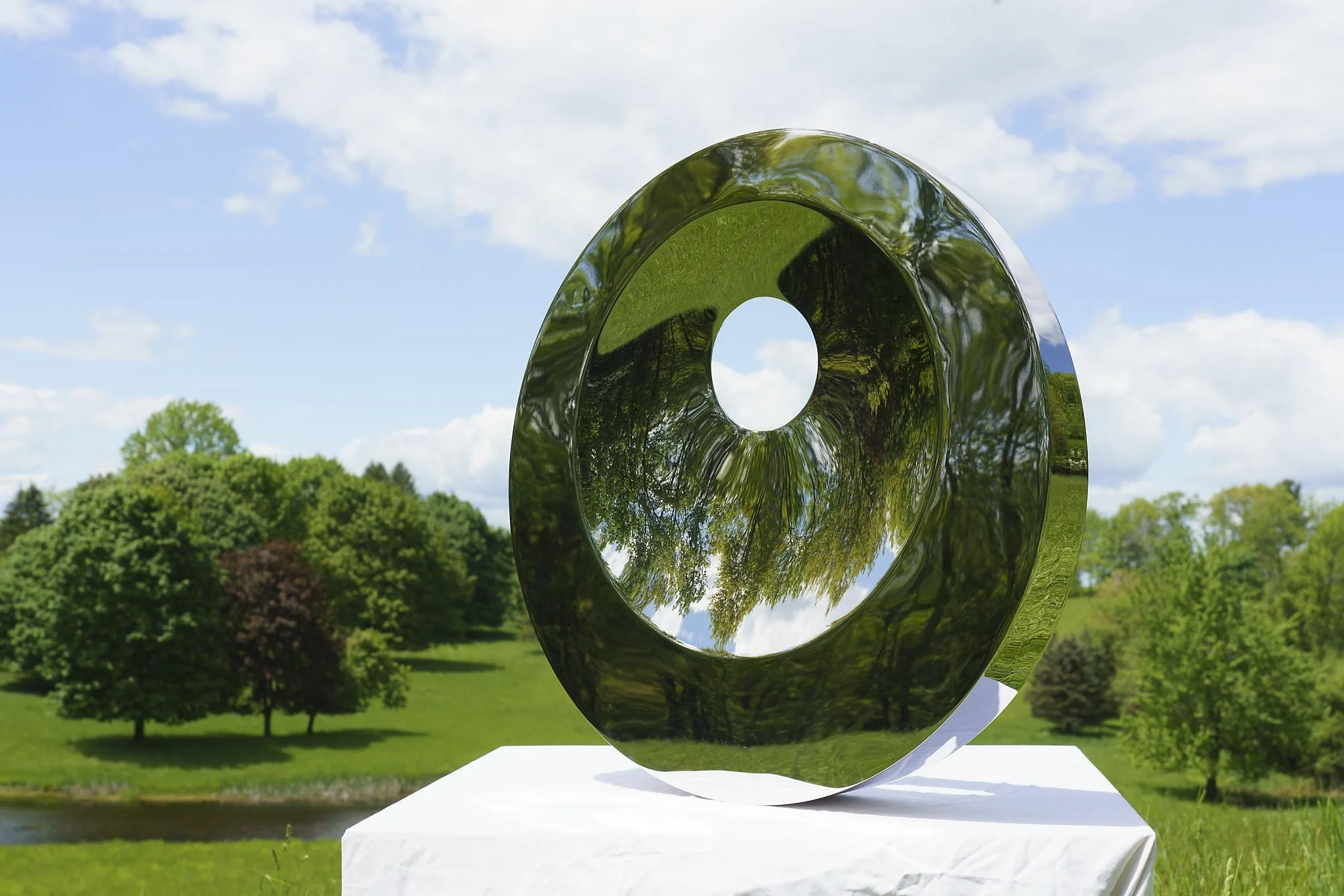 Tarik Currimbhoy’s 316 Stainless steel kinetic sculpture, The Eye, shown from an angle on a white pedestal.