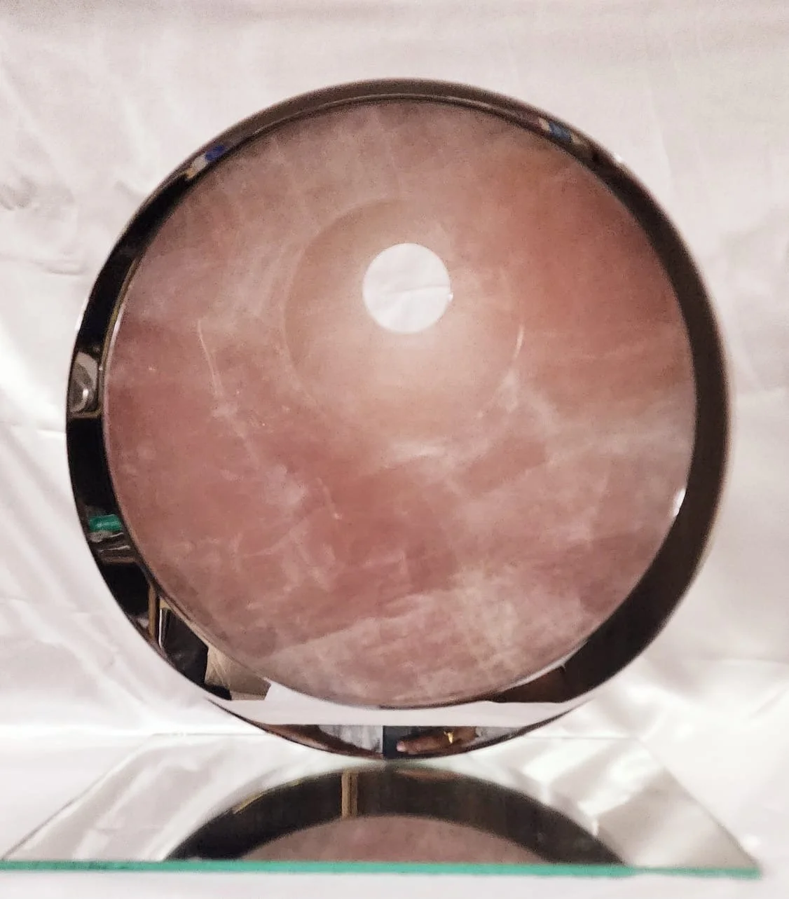 Tarik Currimbhoy’s 316 stainless steel and pink rock kinetic sculpture, Surya, shown from the front. The work rests on a reflective surface.