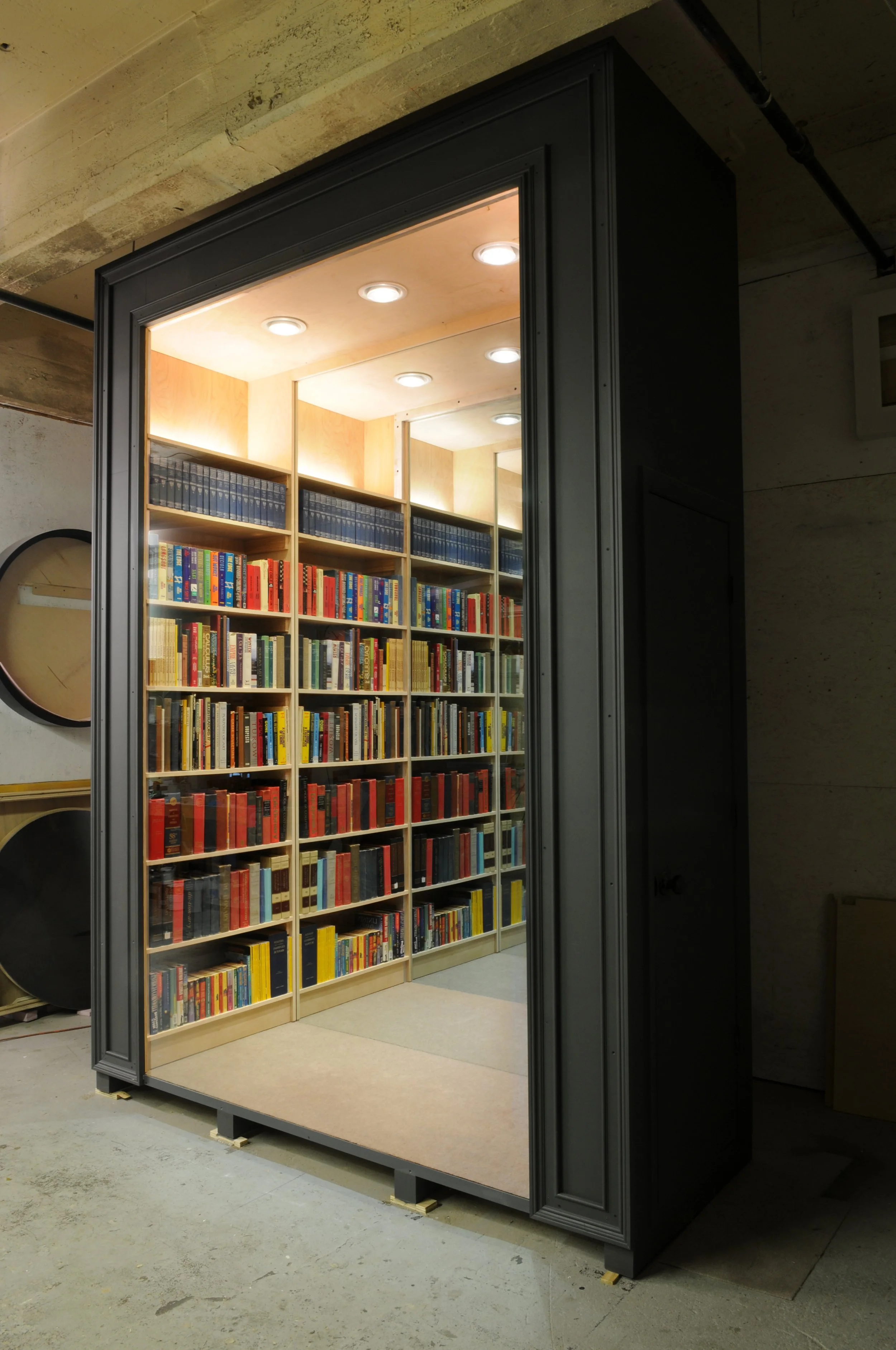 An alternate angle of Chul Hyun Ahn’s 2018 work, 'Library'. The work consists of wood, aluminum, LED lights, books and mirrors. The exterior environment is lit to display the work and its housing in full.