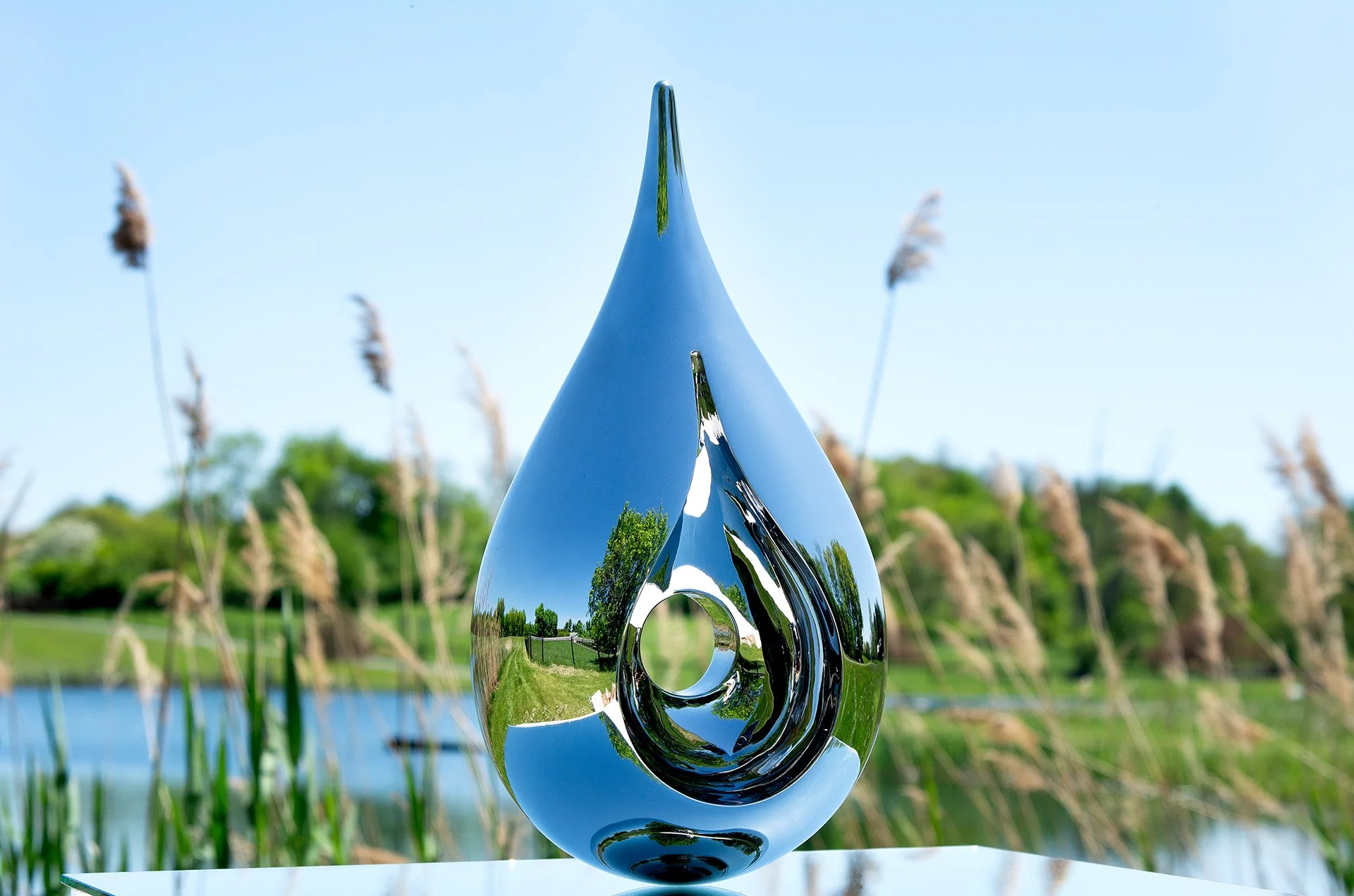 Tarik Currimbhoy’s kinetic stainless steel sculpture, 'Paisley', shown on top of a mirrored base against a natural backdrop.
