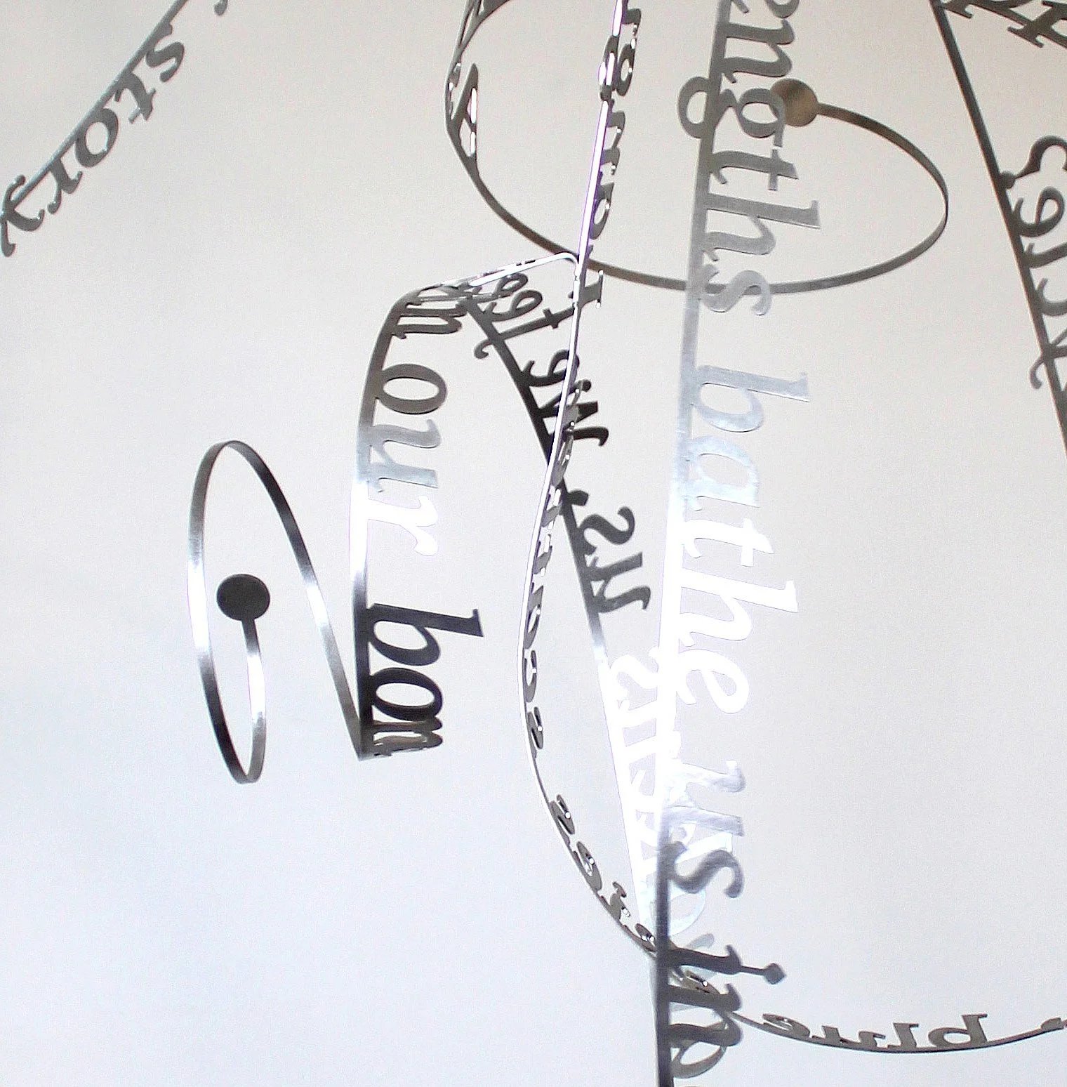 A detail image of Nicola Anthony’s 'Sun dance', a kinetic stainless steel sculpture. The work is shown here suspended from the ceiling against a white backdrop.