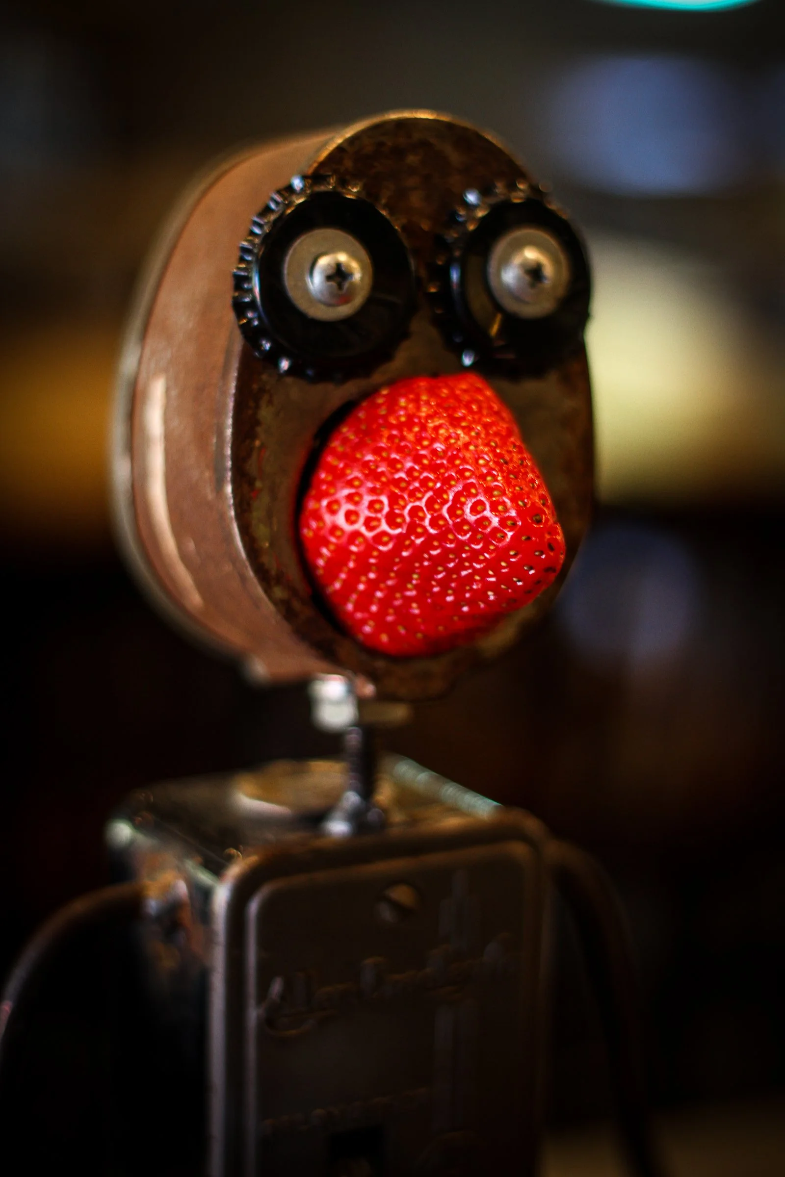 A robot with two black eyes made of camera lenses and a red strawberry as a nose.
