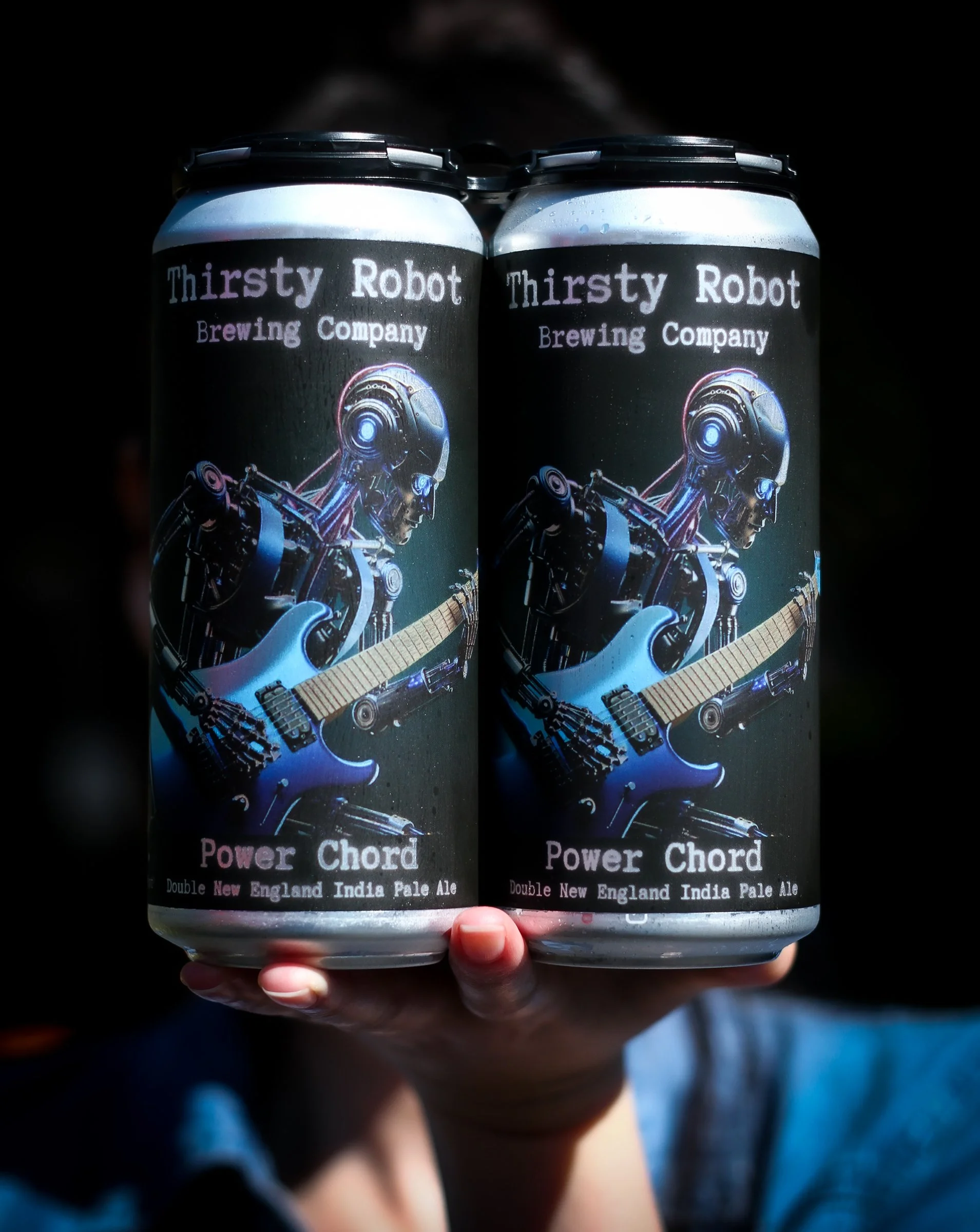 Two cans of Thirsty Robot Brewing Company Power Chord Pale Ale being held in a person's hand.