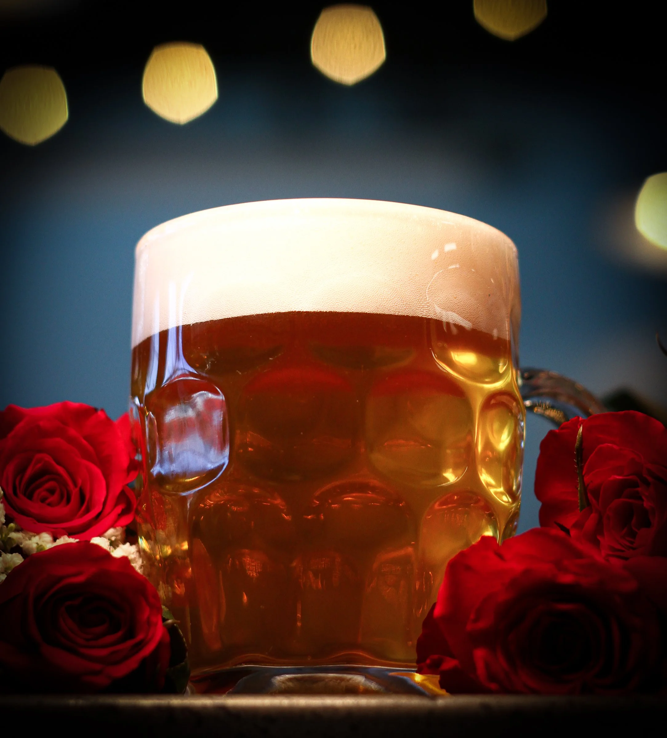 A glass of beer with a foam head, surrounded by red roses.