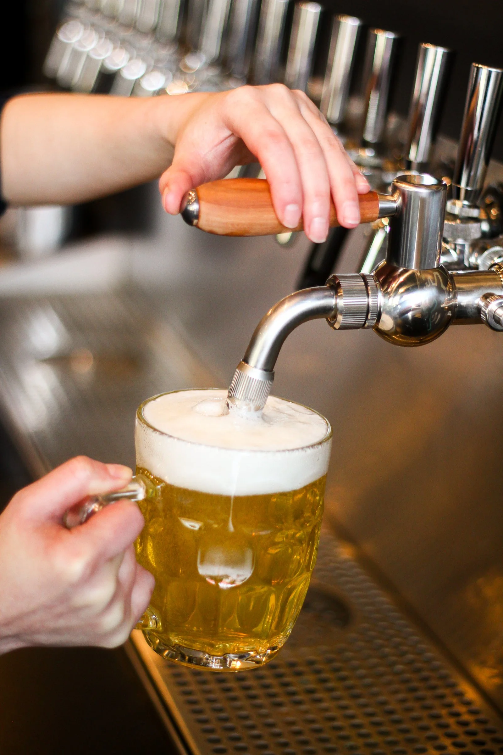 A person is pouring beer from a tap into a glass mug at a bar.