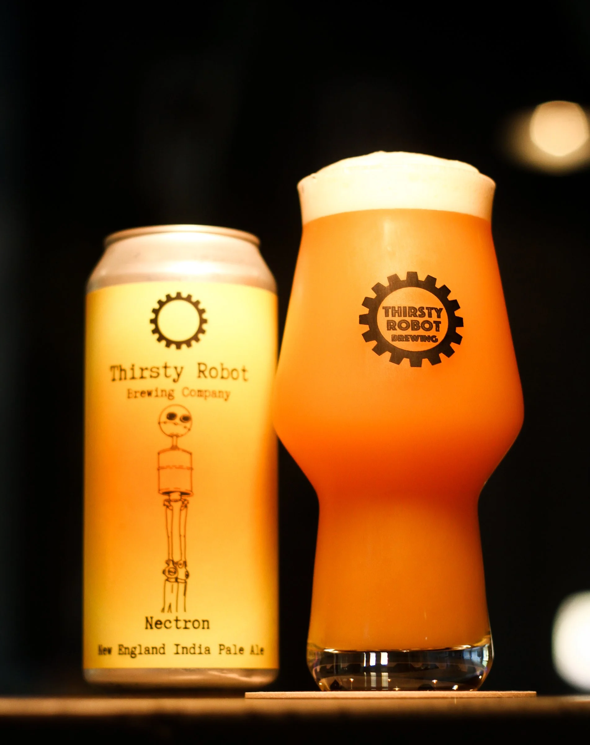 A can of Thirsty Robot brewing company's Neutron New England India Pale Ale next to a glass of beer with a frothy head, both featuring Thirsty Robot logos, against a dark background.