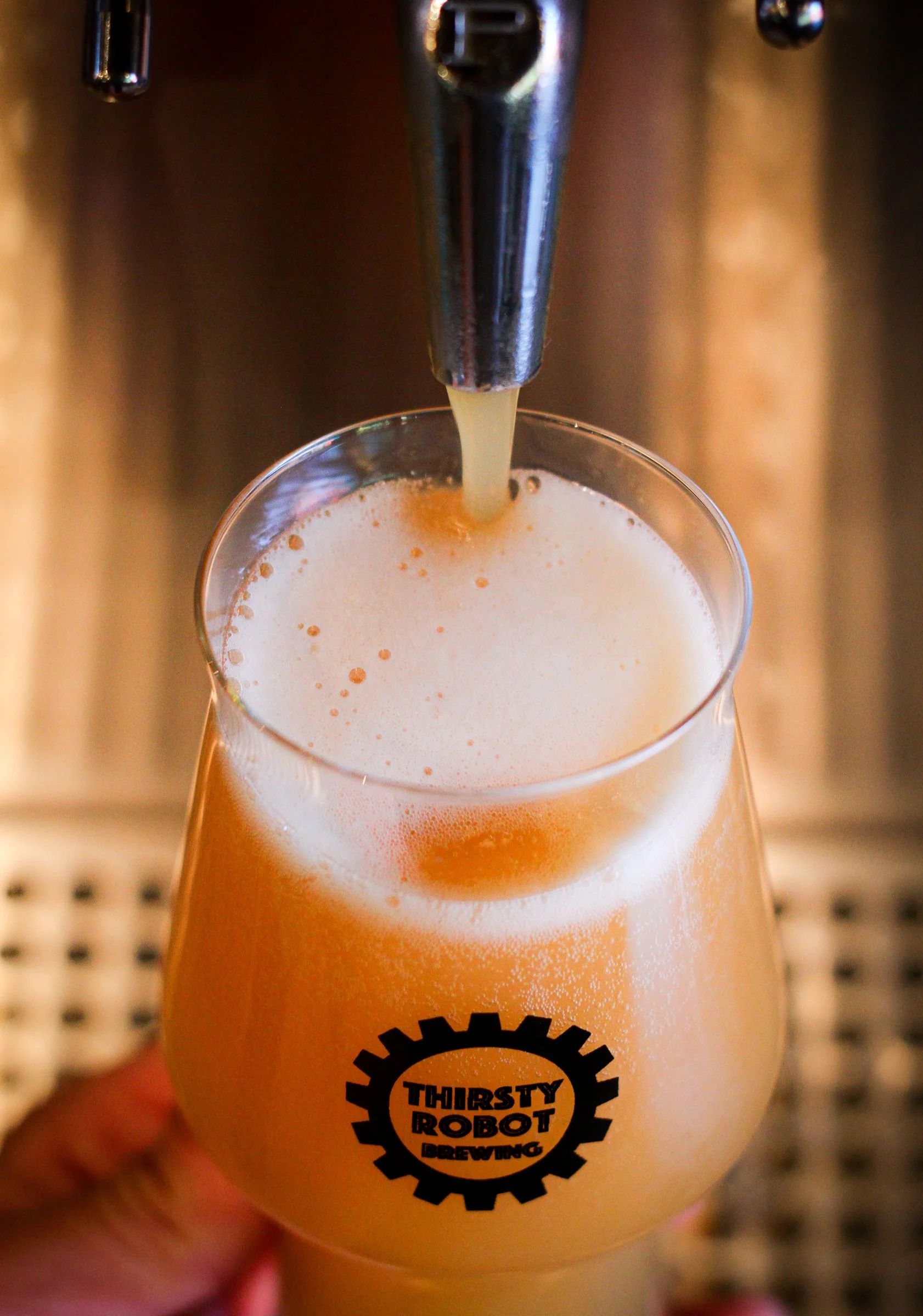A glass of beer being filled from a tap, with the logo 'Thirsty Robot Brewing' on the glass.
