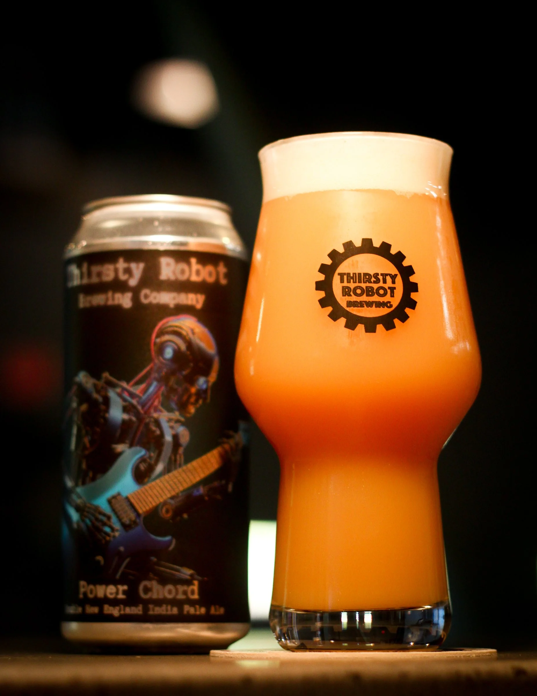 A can of Thirsty Robot Brewing Company Power Chord India Pale Ale and a glass of beer with Thirsty Robot logo, on a dark surface.
