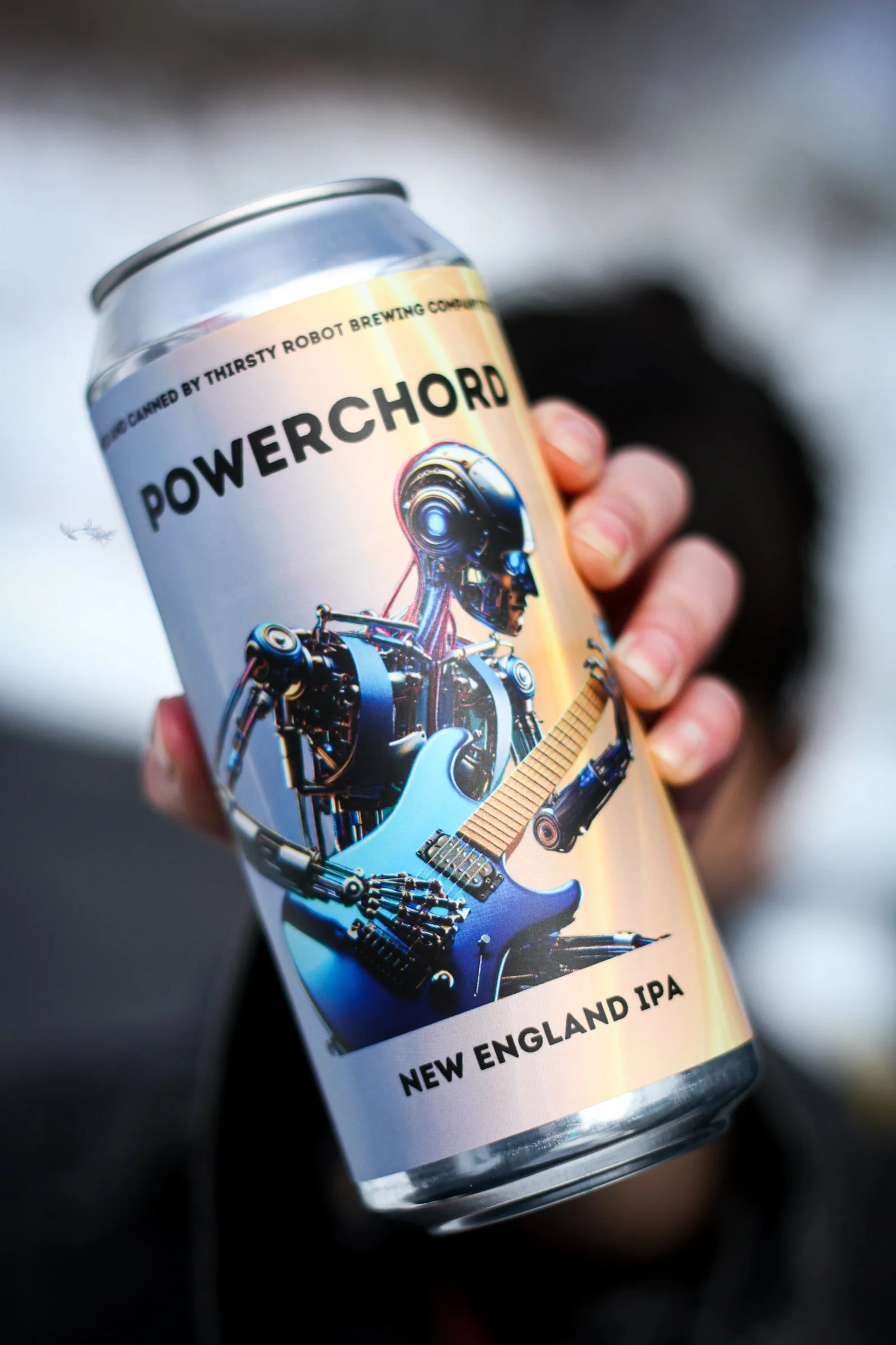 A person holding a can of Powerchord New England IPA beer with robot and guitar artwork on the label.