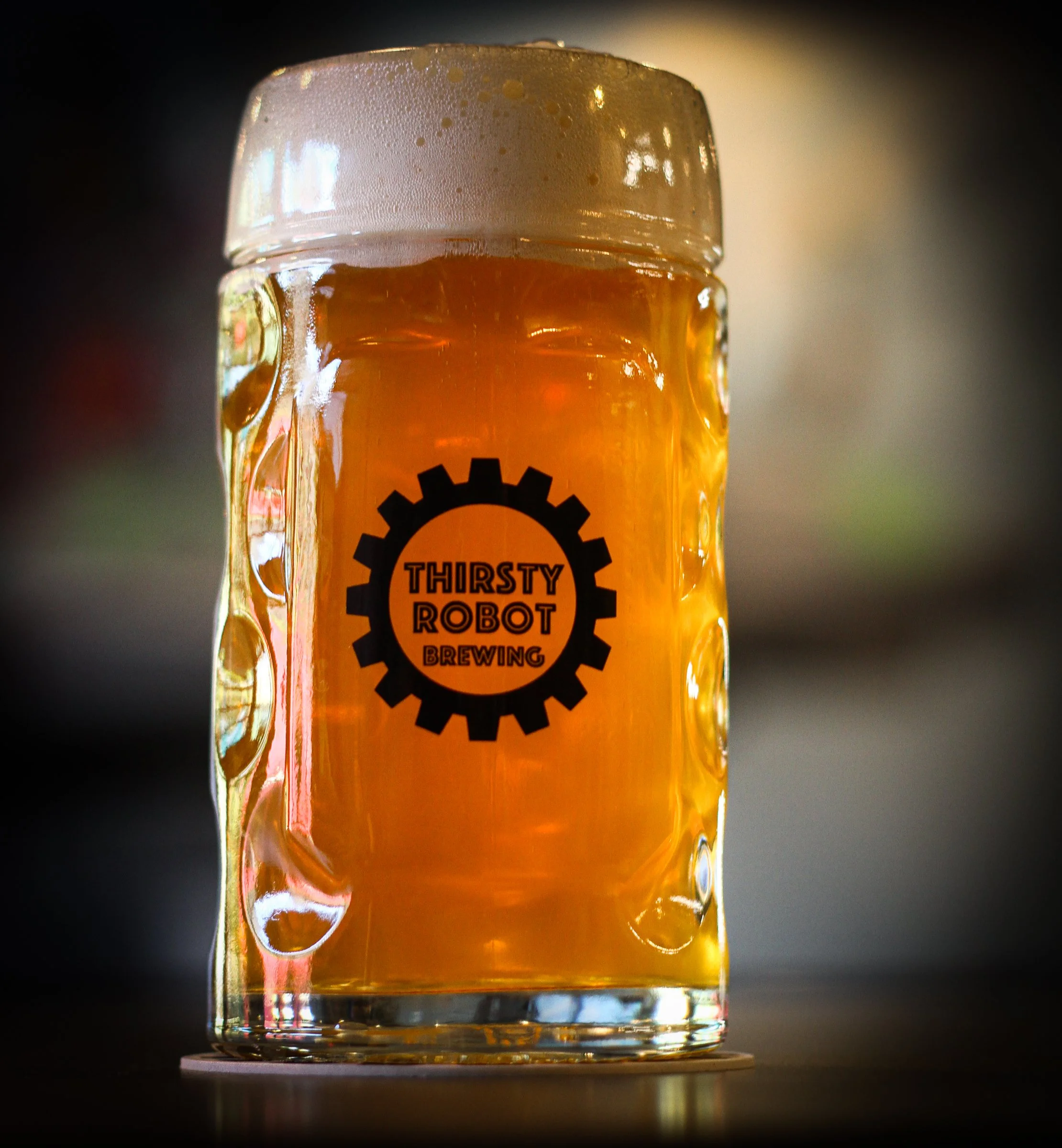 A glass of beer with foam on top, featuring a logo that says 'Thirsty Robot Brewing' with a gear design.
