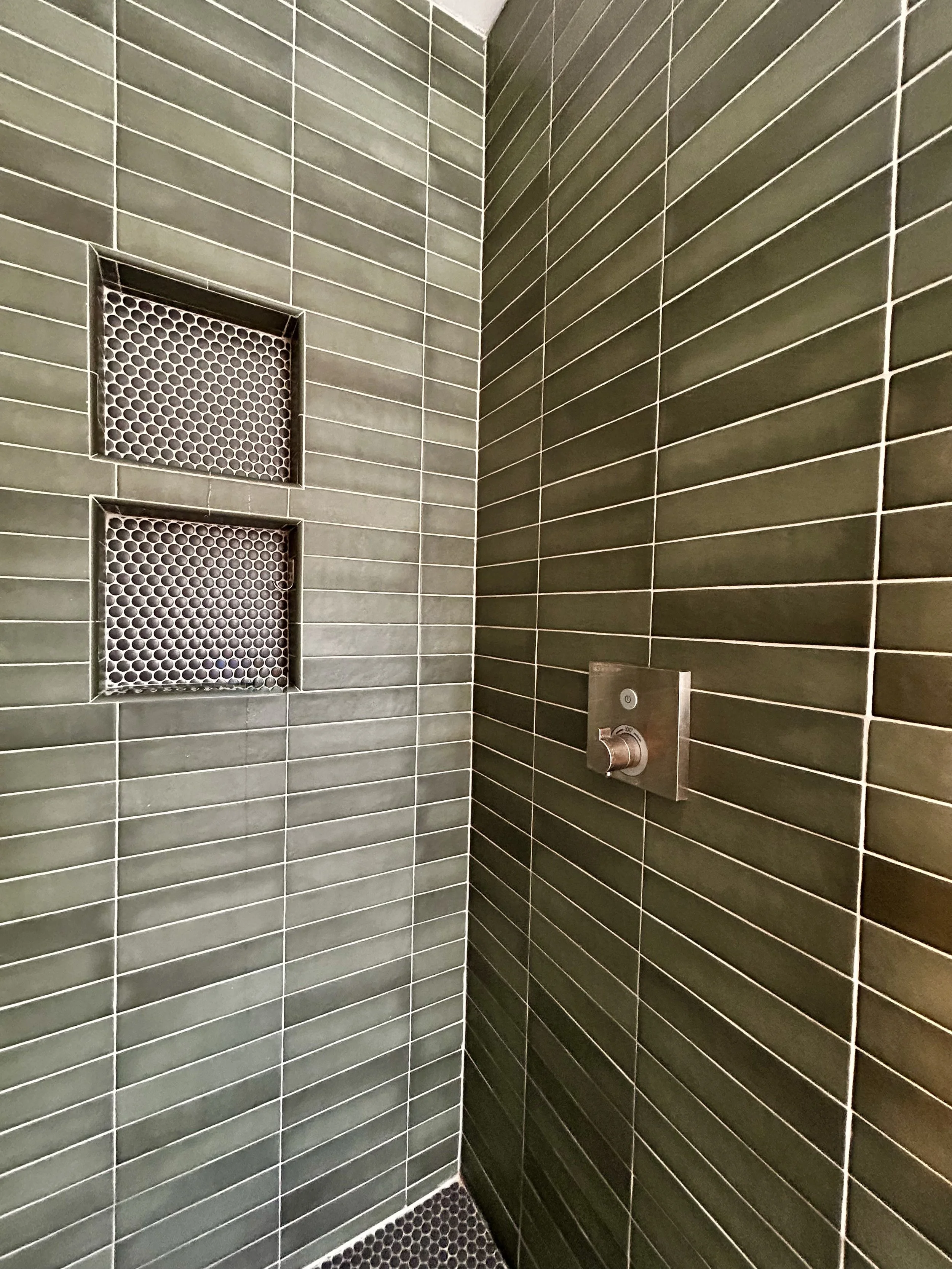 Sage green subway tile shower, tile stacked horizontally with gray penny tile niches