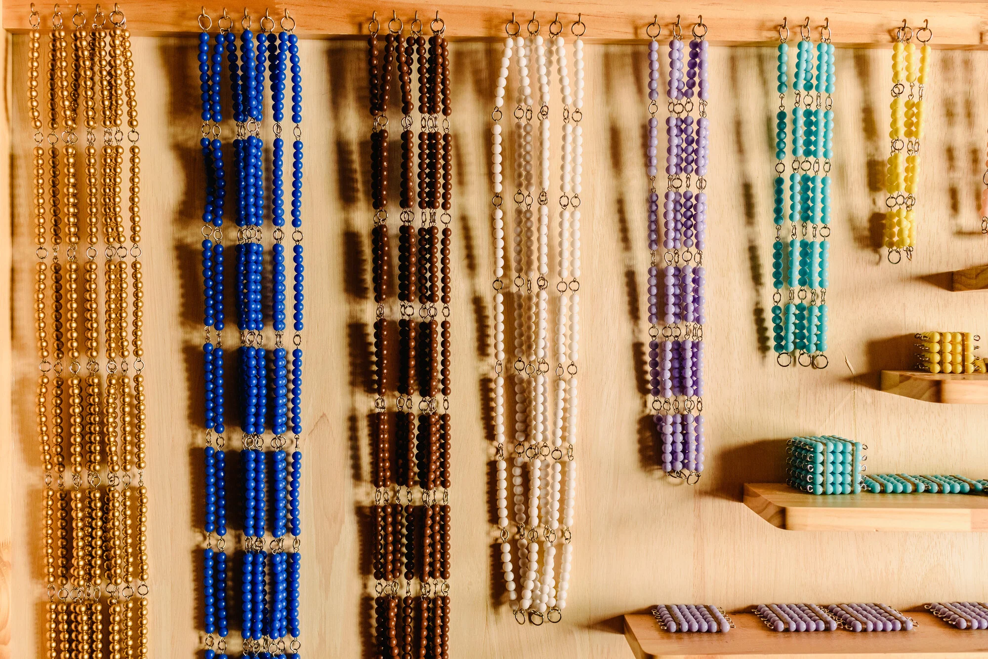 Colorful montessori beads hanging on wooden display racks for porirua montessori