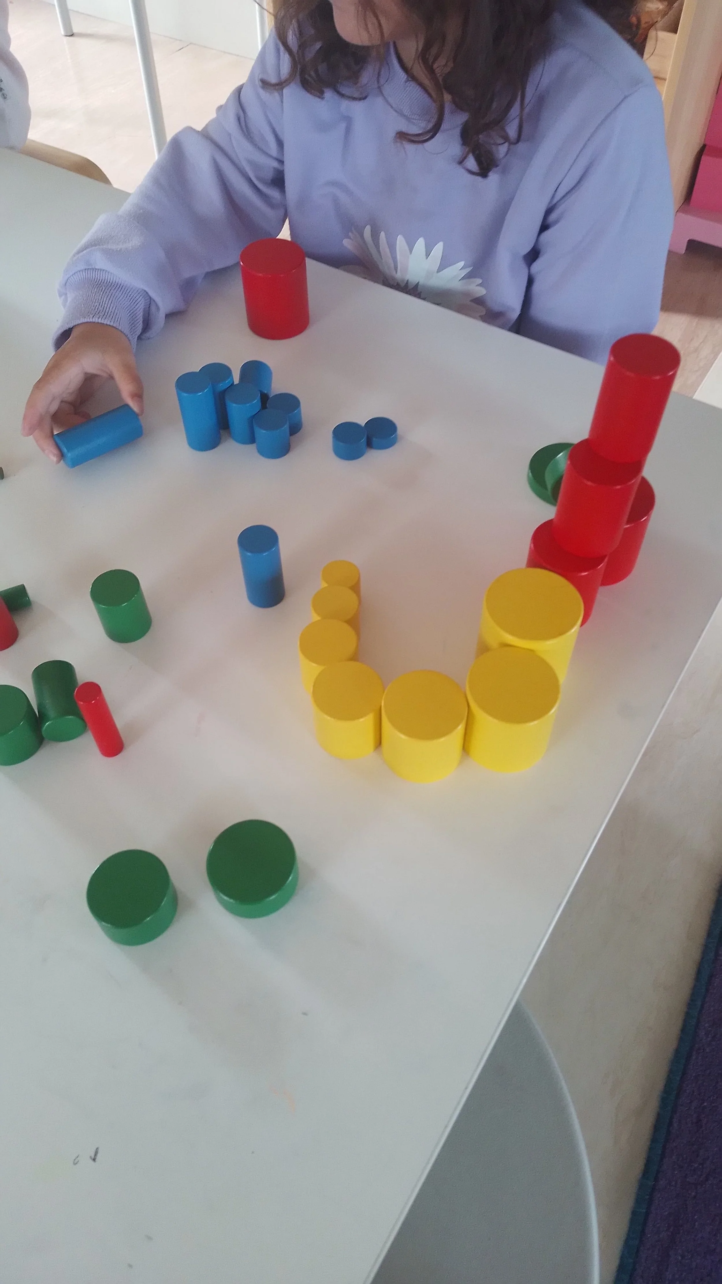 Child playing with knobless cylinders learning about dimensions, patterning and concentration at porirua montessori.