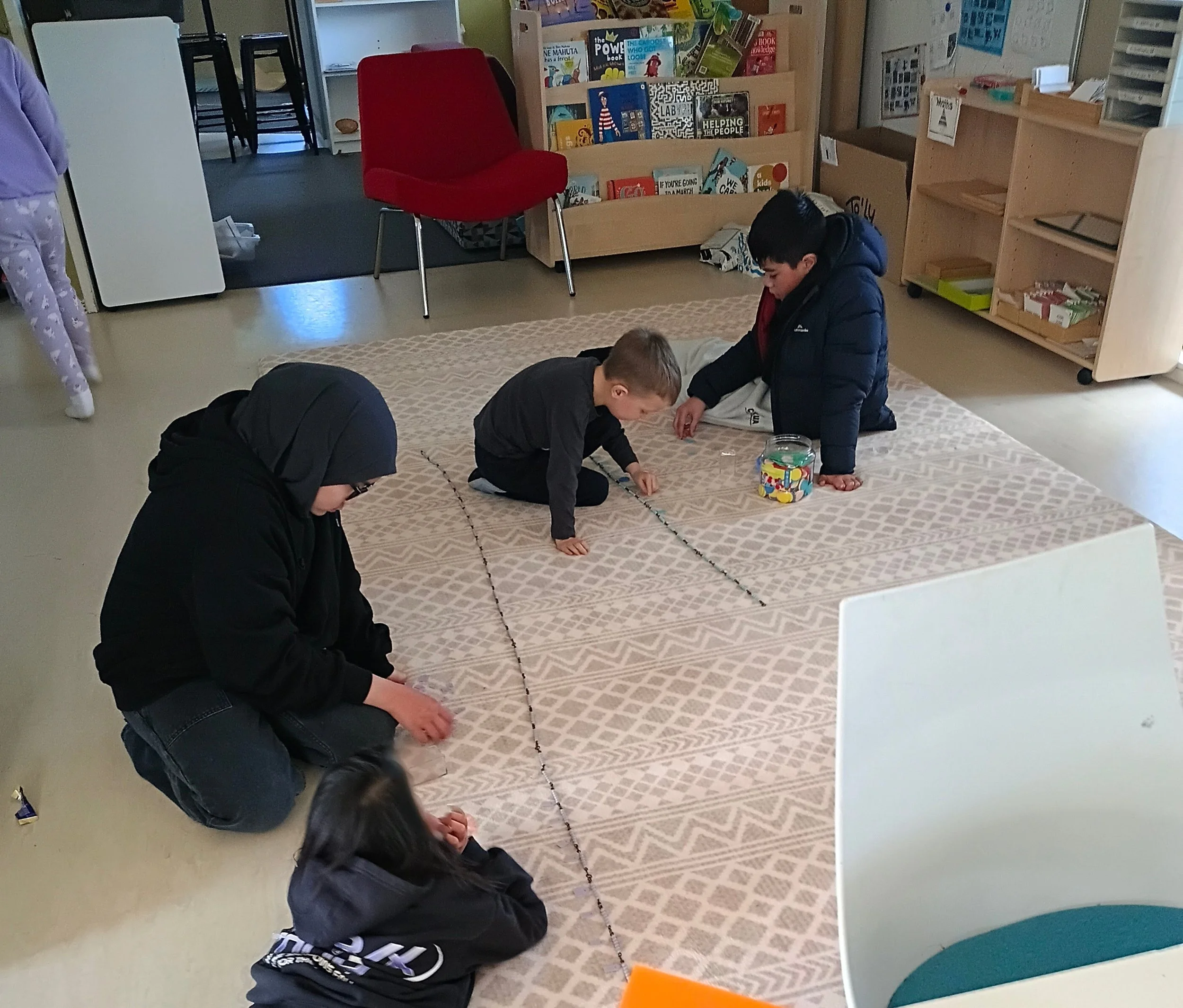 Children working together with materials on a large floor mat in the Porirua Montessori classroom