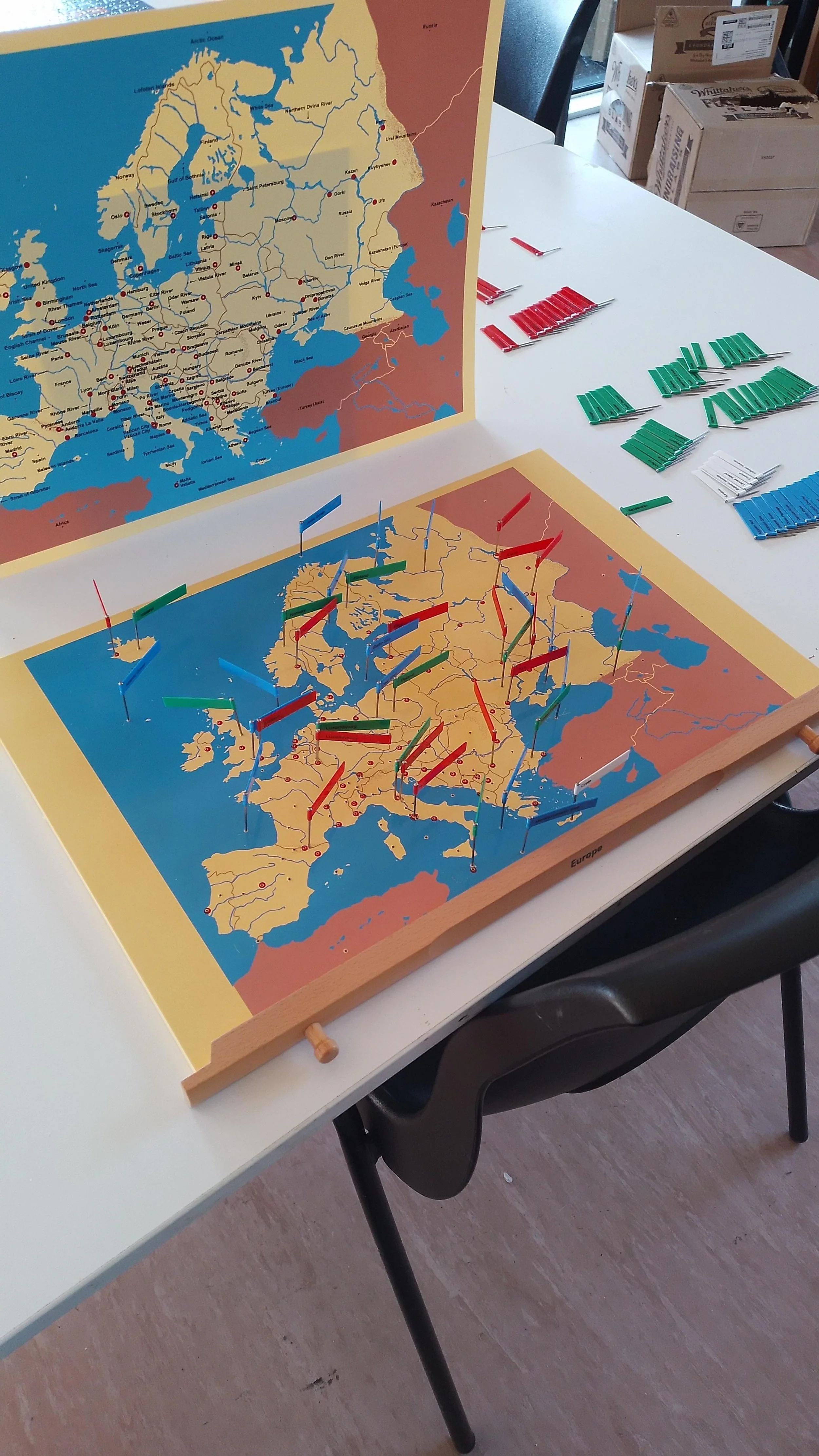 A Europe-themed board game with map, colored flags, and green, red, and blue game pieces and cards on a white table.