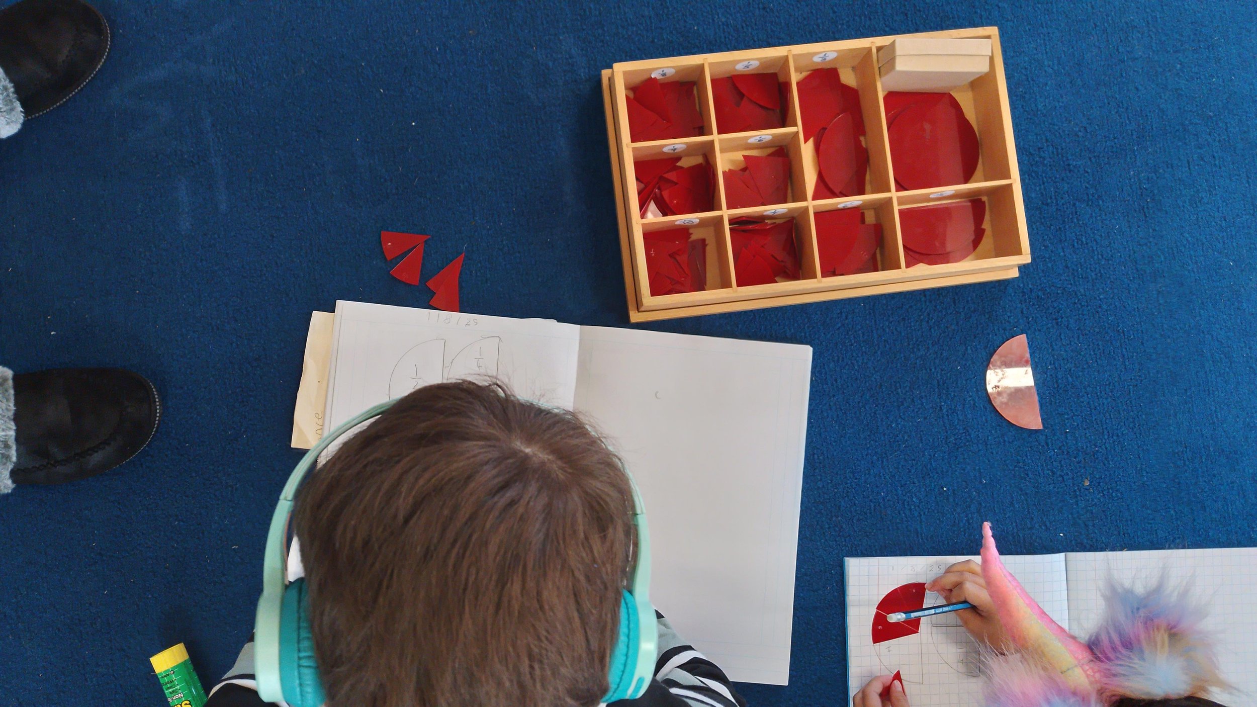 Children working on a math activity with red paper semicircles and a wooden organizer on a blue carpet.