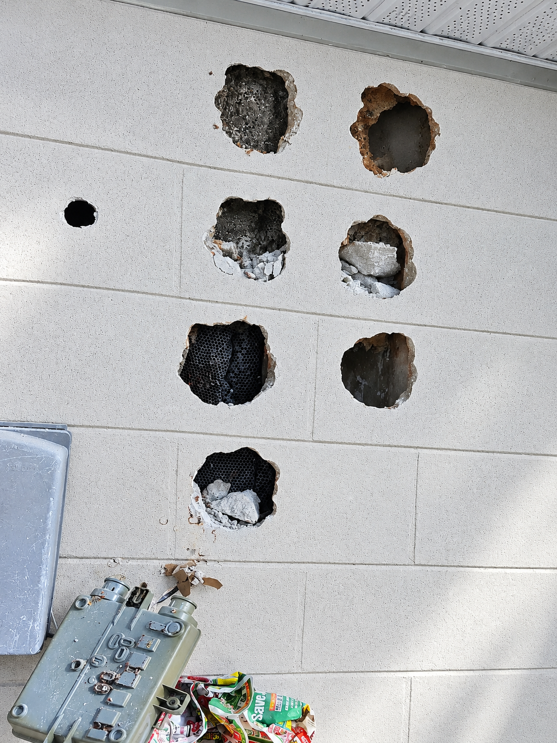 Damaged concrete wall with multiple holes and exposed mesh.