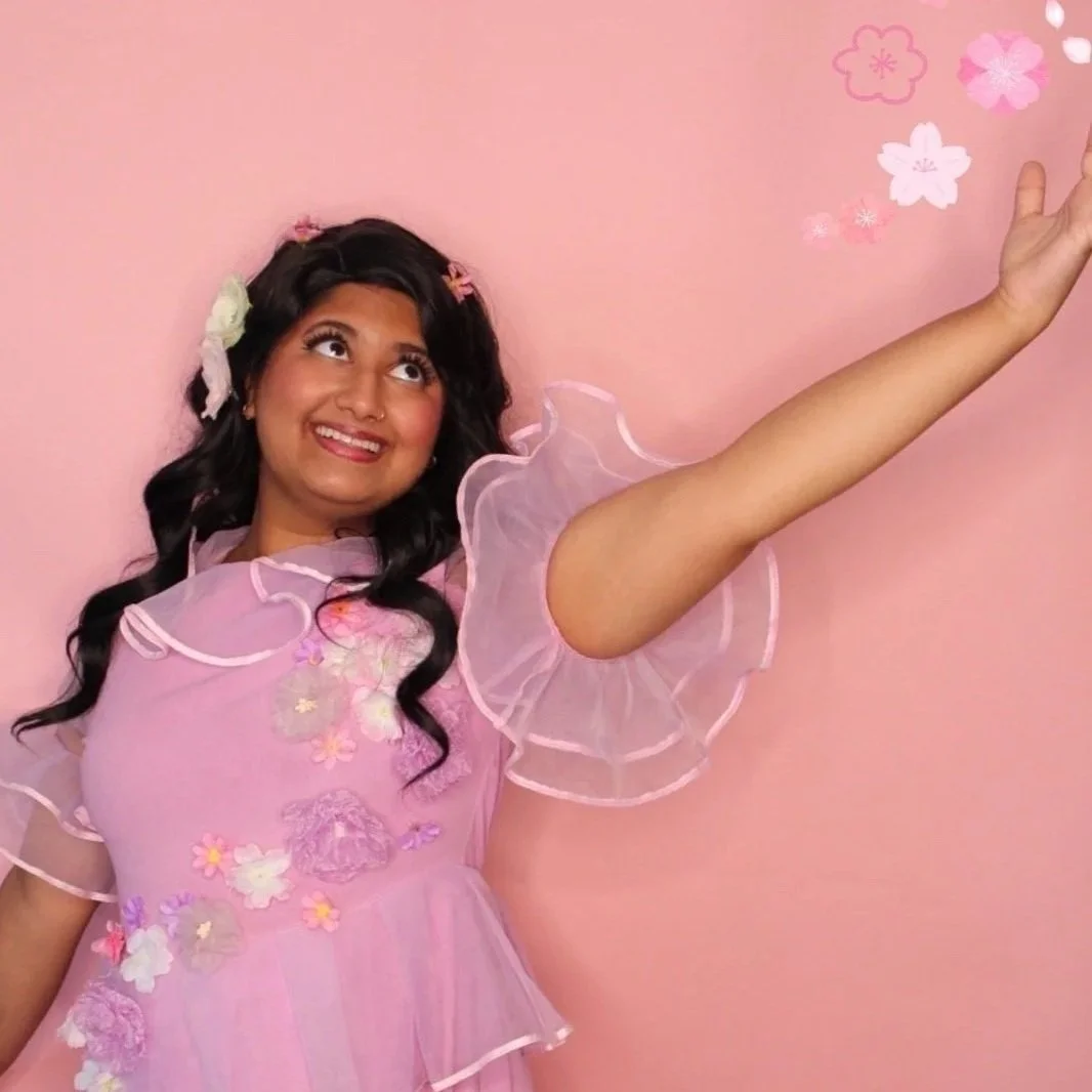 Princess wearing a pink dress covered in flowers with long wavy black hair looks to the upper right corner