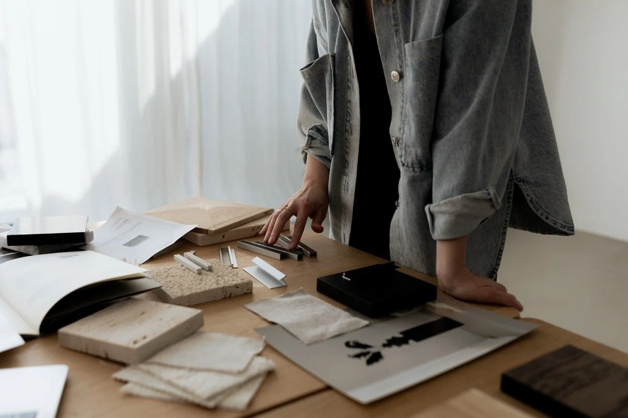 A person standing at a table that's covered in tile samples, fabrics, pictures, and magazines.
