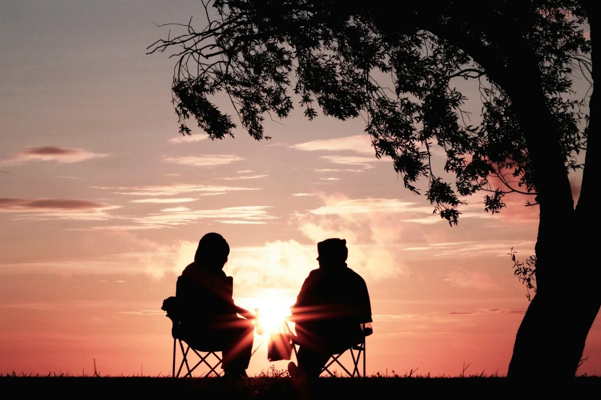 Two people gathered around a fire at sunset, reflecting the ancient tradition of storytelling, presence, and human connection.