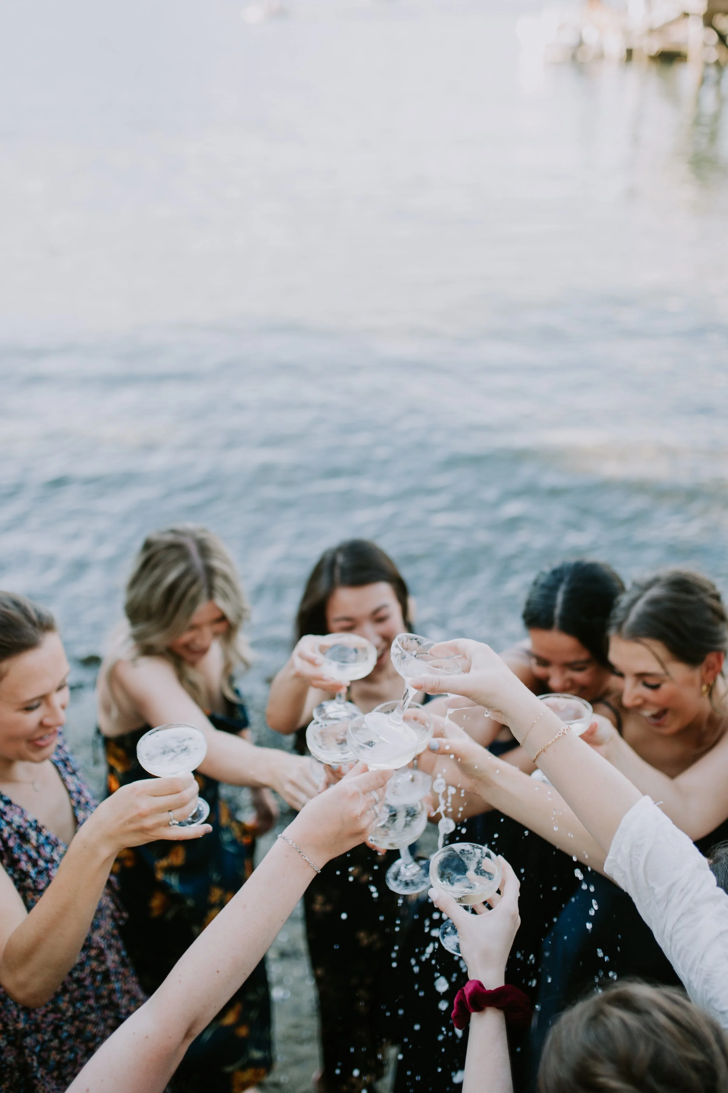 Group of people toasting with champagne glasses near water.