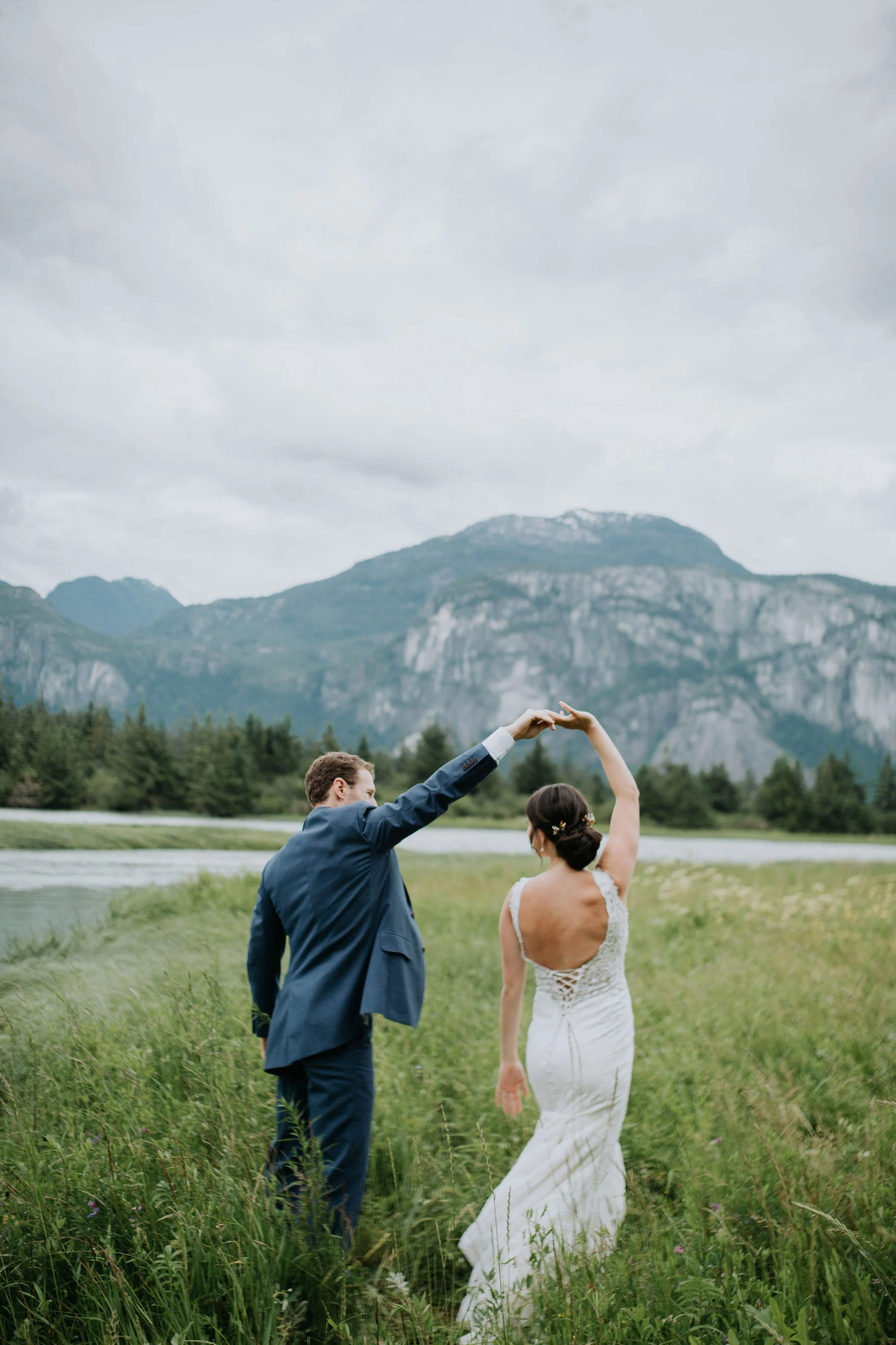 Bride and groom dancing in a field with mountains in the background.