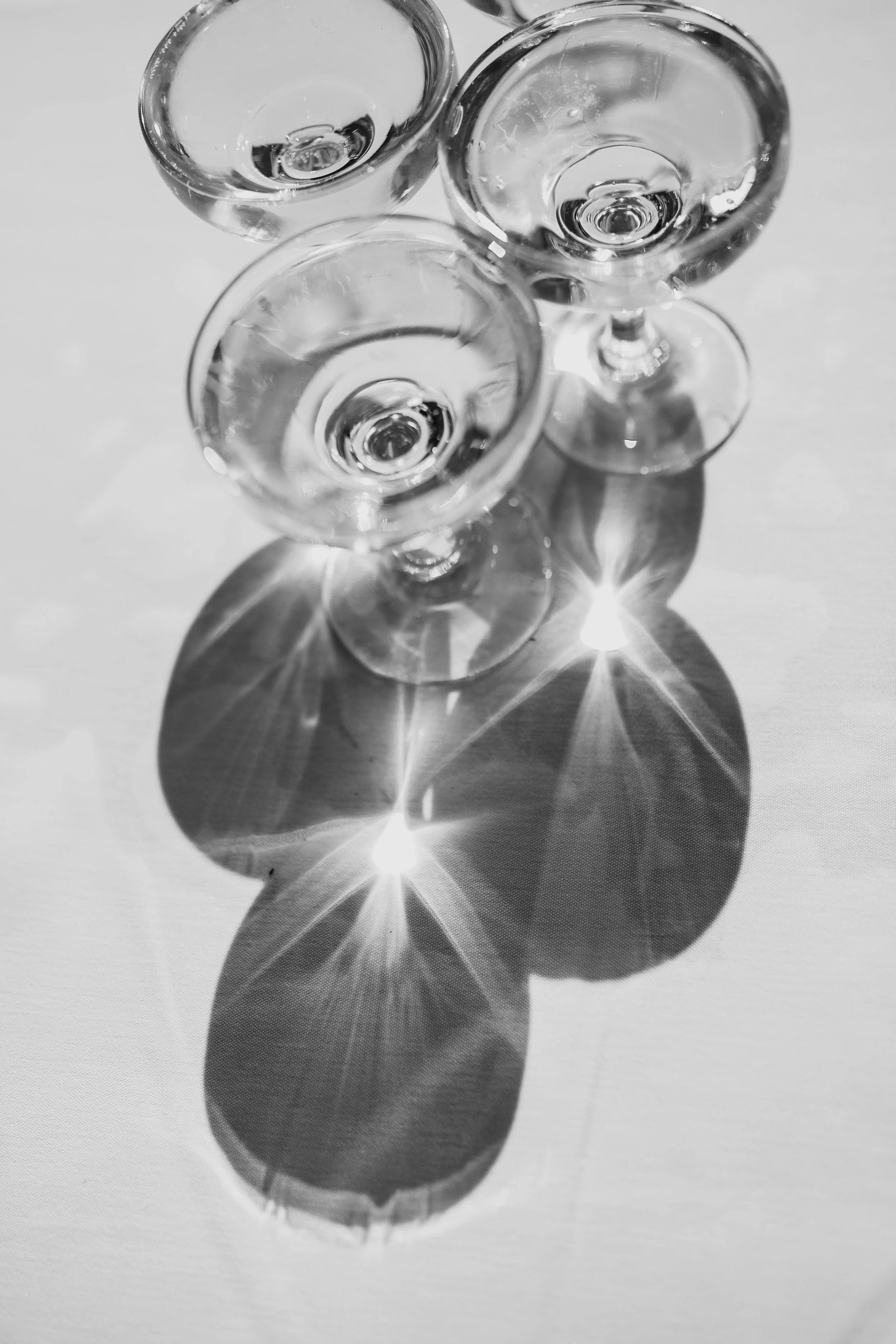 Black and white photo of three empty cocktail glasses with light reflections and shadows on a white surface.