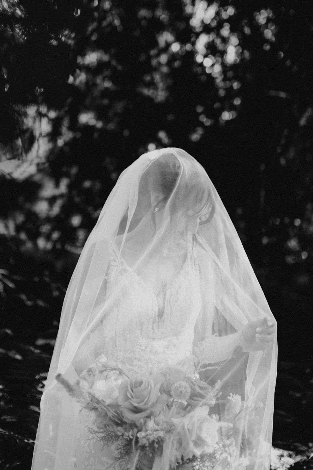 Black and white photo of a bride with a veil, holding a bouquet of flowers.
