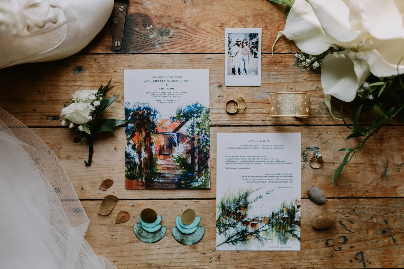 Wedding invitation suite on wooden table with flowers, rings, and jewelry.