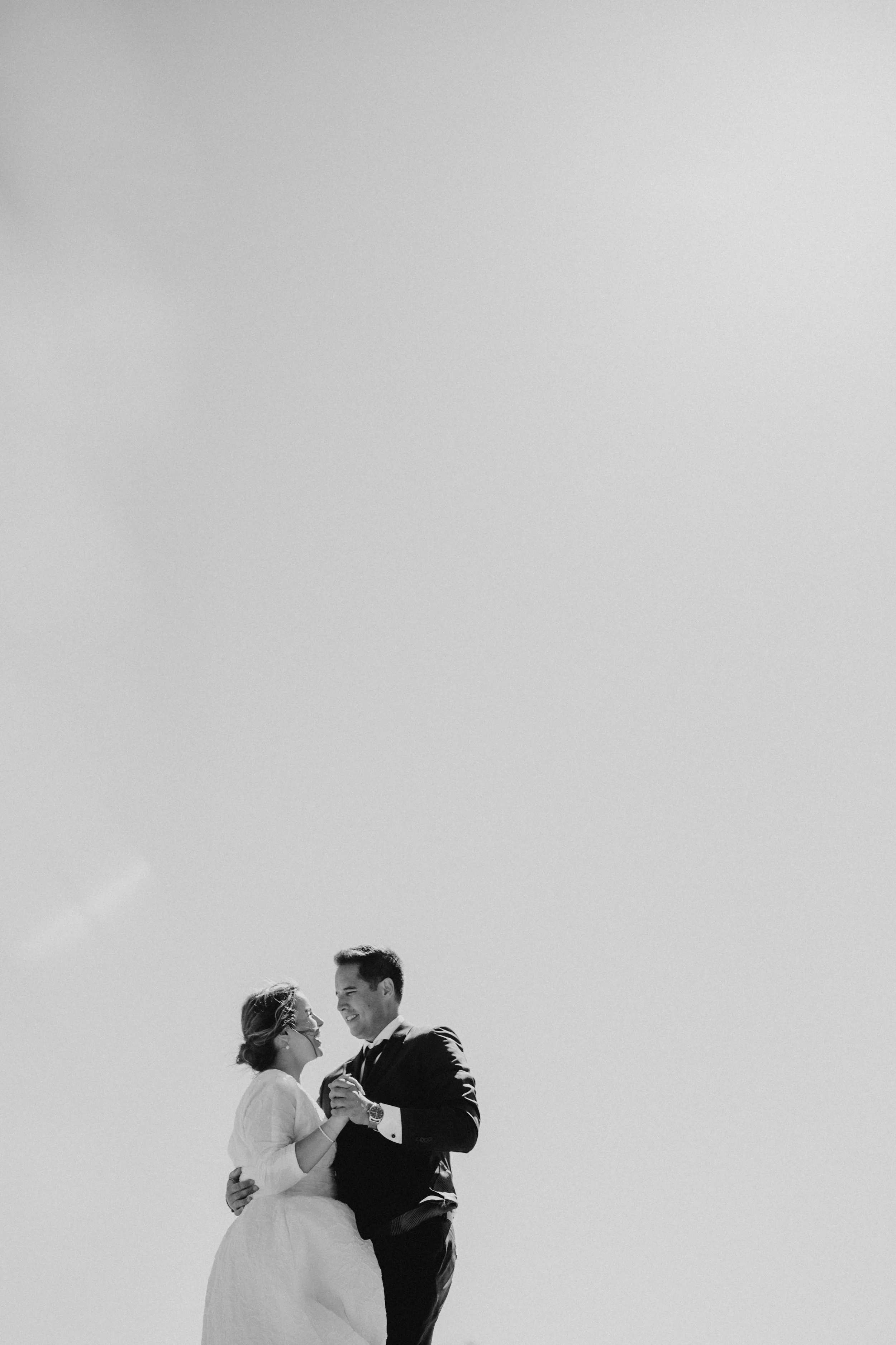 Black and white photo of a couple dancing in wedding attire against a clear sky.