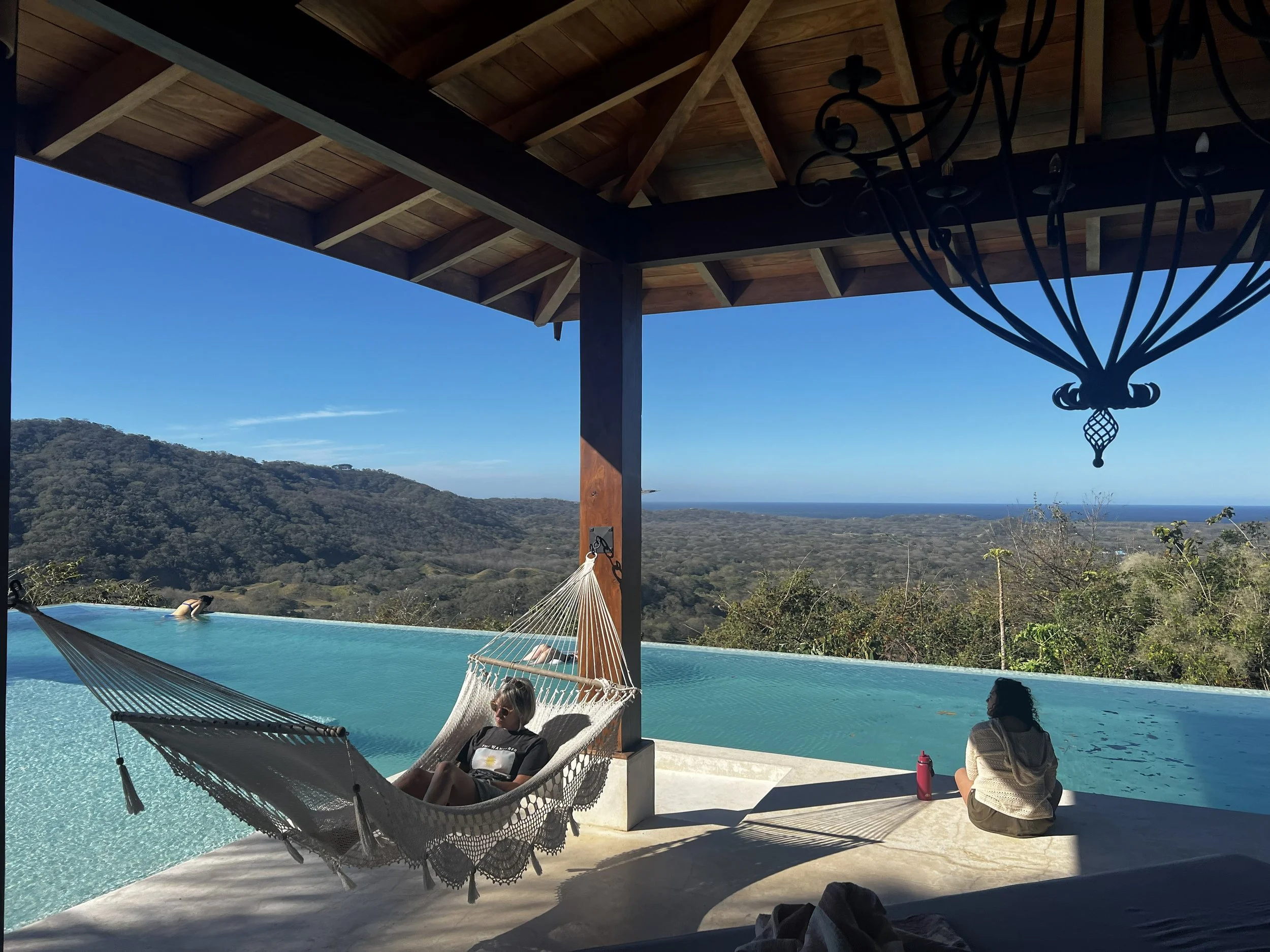 Women relaxing on the hammock  beside the infinity swimming pool with a scenic mountain and ocean view in the background at the women's ayahuasca retreat.