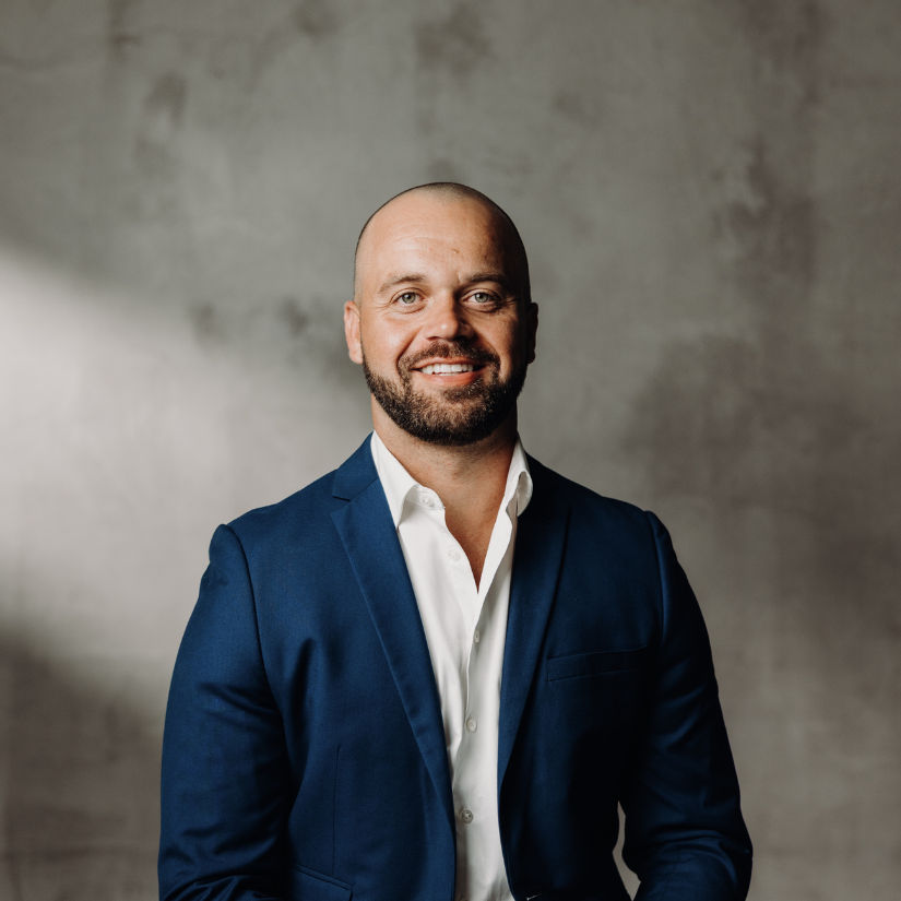 Eden Appo, Operations Manager at The Srama Group in a suit and dress shirt against a vine-covered brick wall