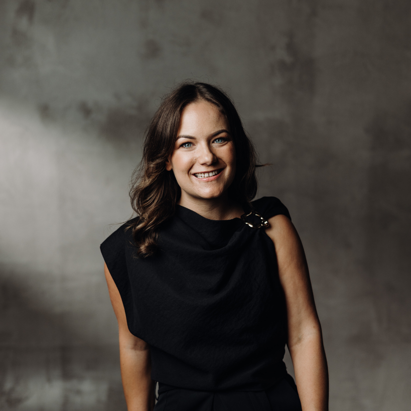 Olivia McCrea, Buyers Agent at The Srama Group in a suit and dress shirt against a vine-covered brick wall