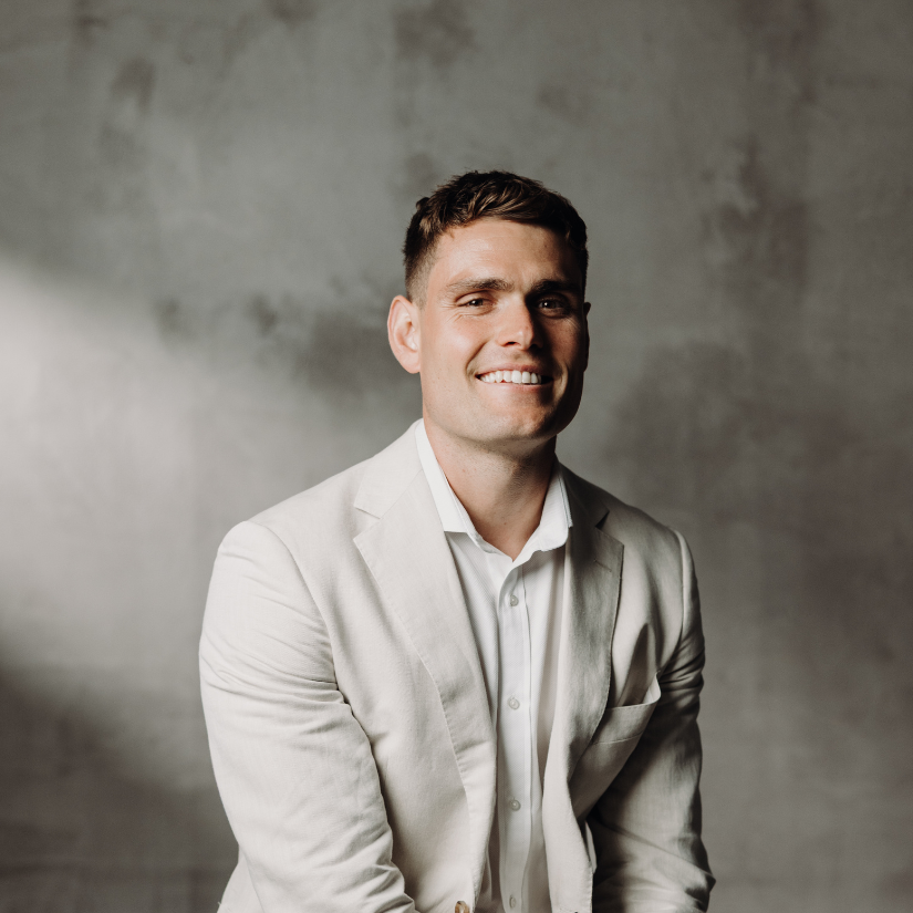 Brandon Doran, Buyers Agent at The Srama Group in a suit and dress shirt against a vine-covered brick wall