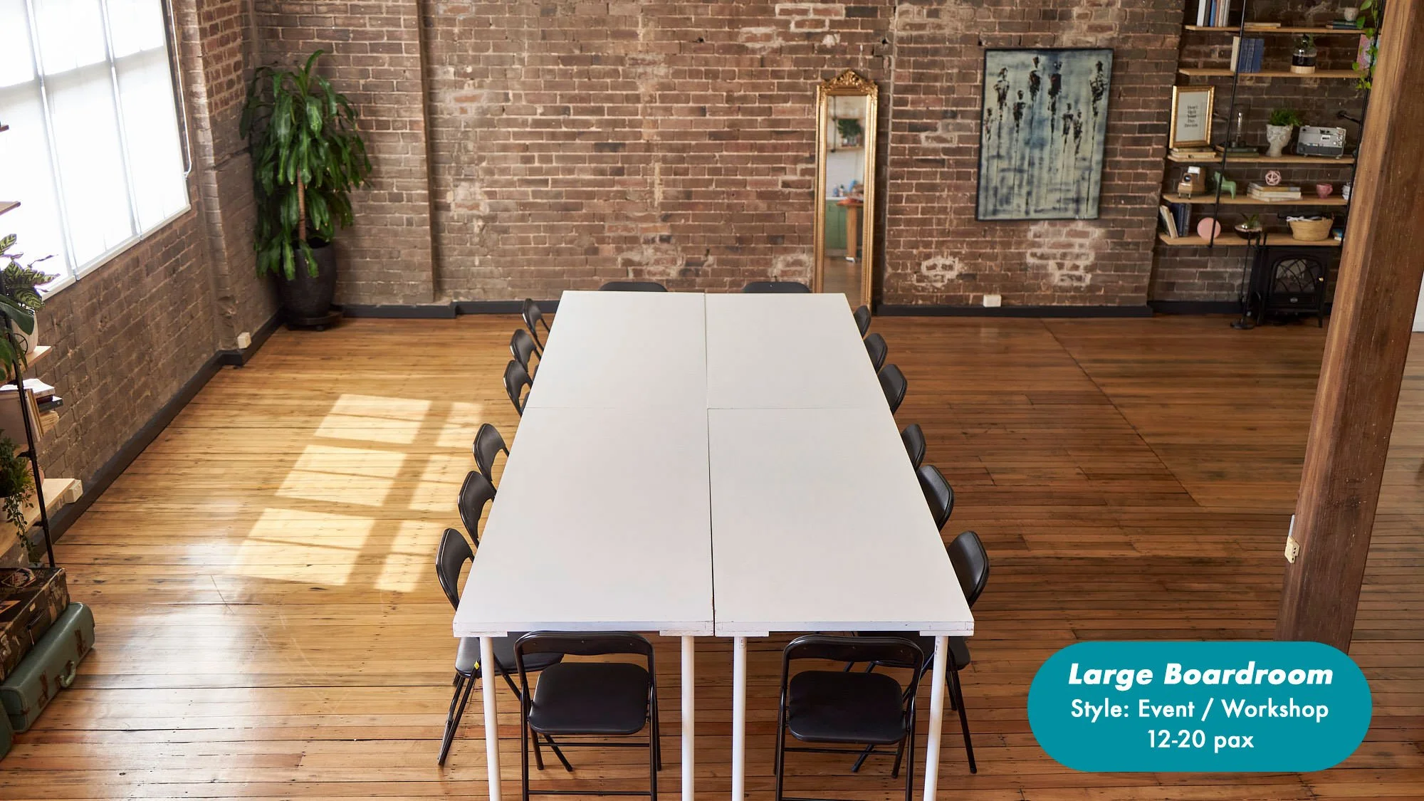 Large brick-walled boardroom with a long white workshop table, folding chairs, hardwood floors, plants, shelving, and wall art; seats 12–20 people at the Dale Studio in Chippendale. 