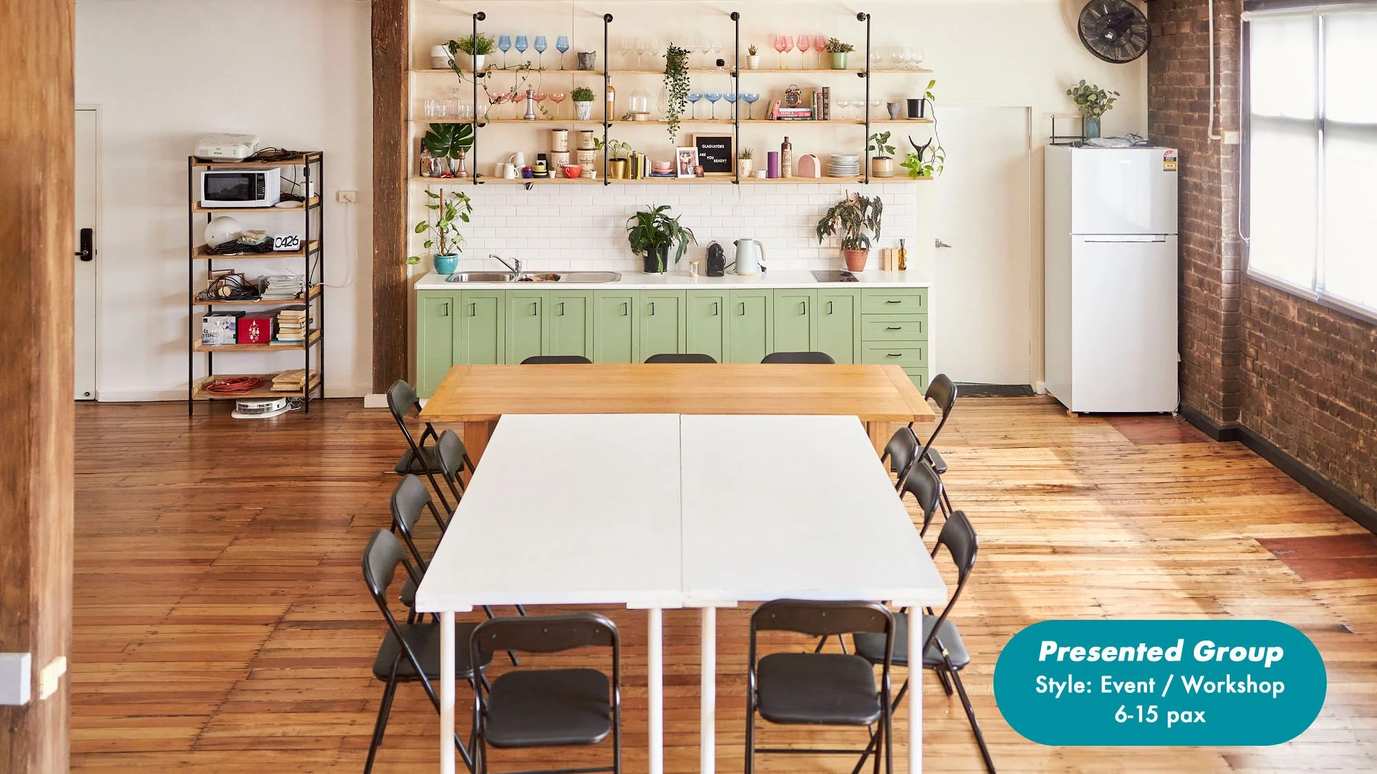 Bright event workshop space with a long table, folding chairs, green kitchen cabinets, open shelves, plants, and refrigerator at the Dale Studio in Chippendale. 
