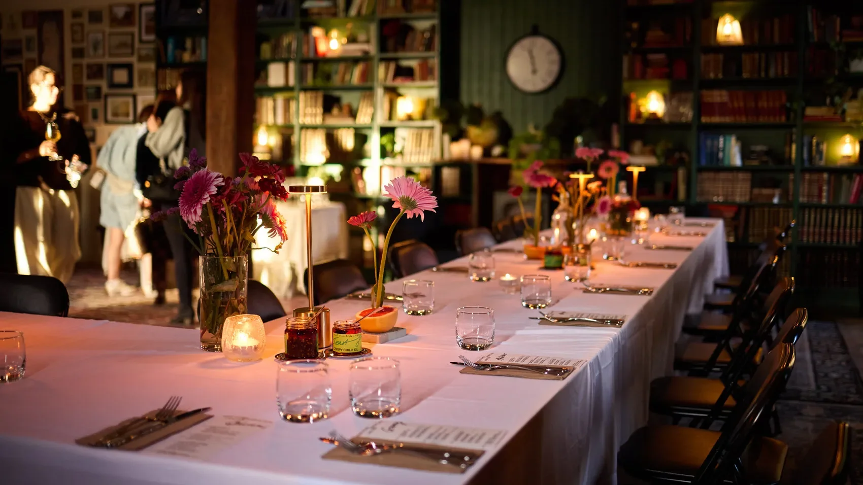 Elegant restaurant dining room with a long white-tablecloth table, flowers, candles, place settings, and bookshelves at the Dale Library in Chippendale. 