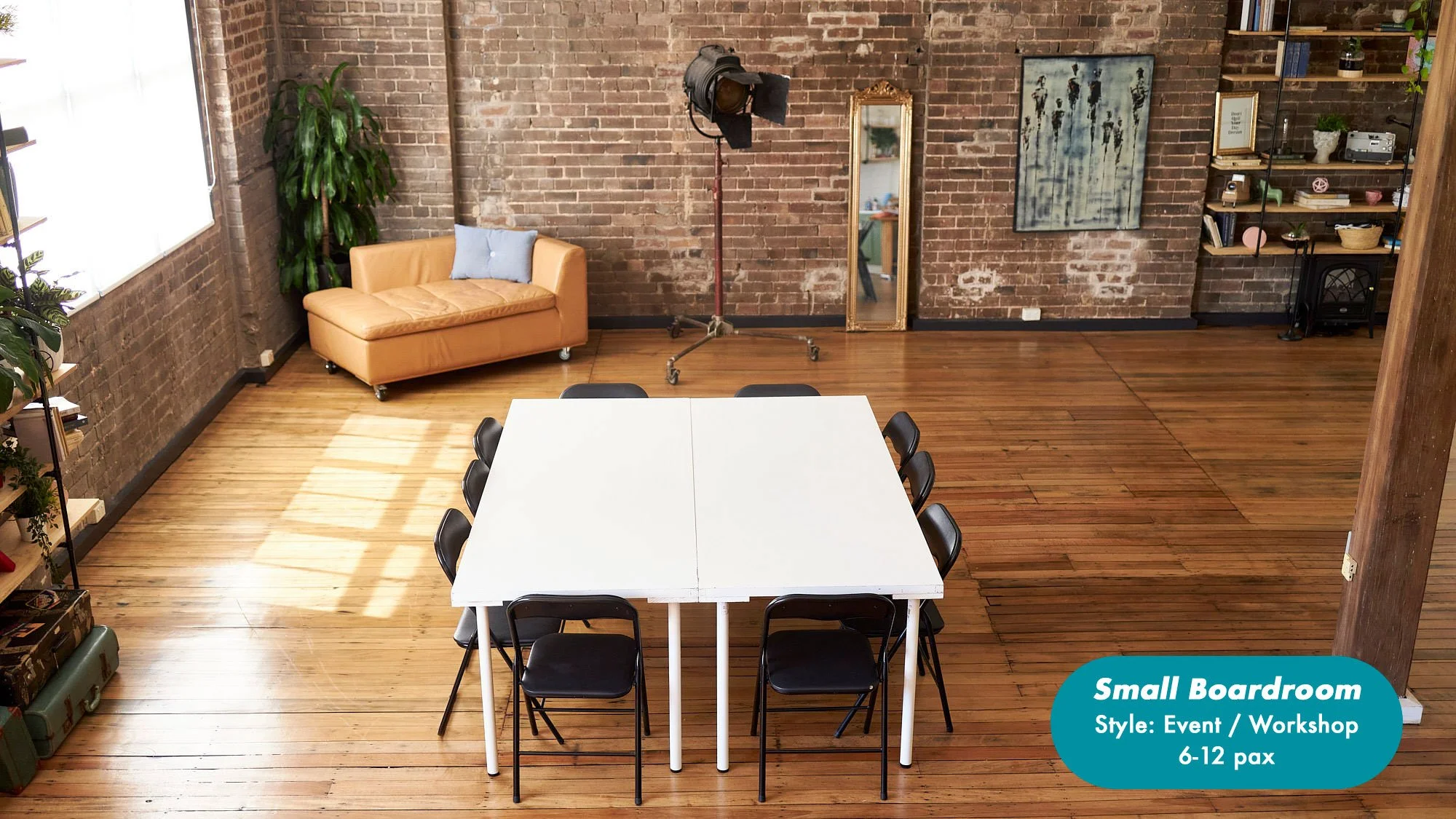 Small brick-walled boardroom with a white conference table, black folding chairs, leather sofa, studio light, mirror, artwork, plants, and shelving; seating for 6–12 people. at the Dale Studio in Chippendale. 