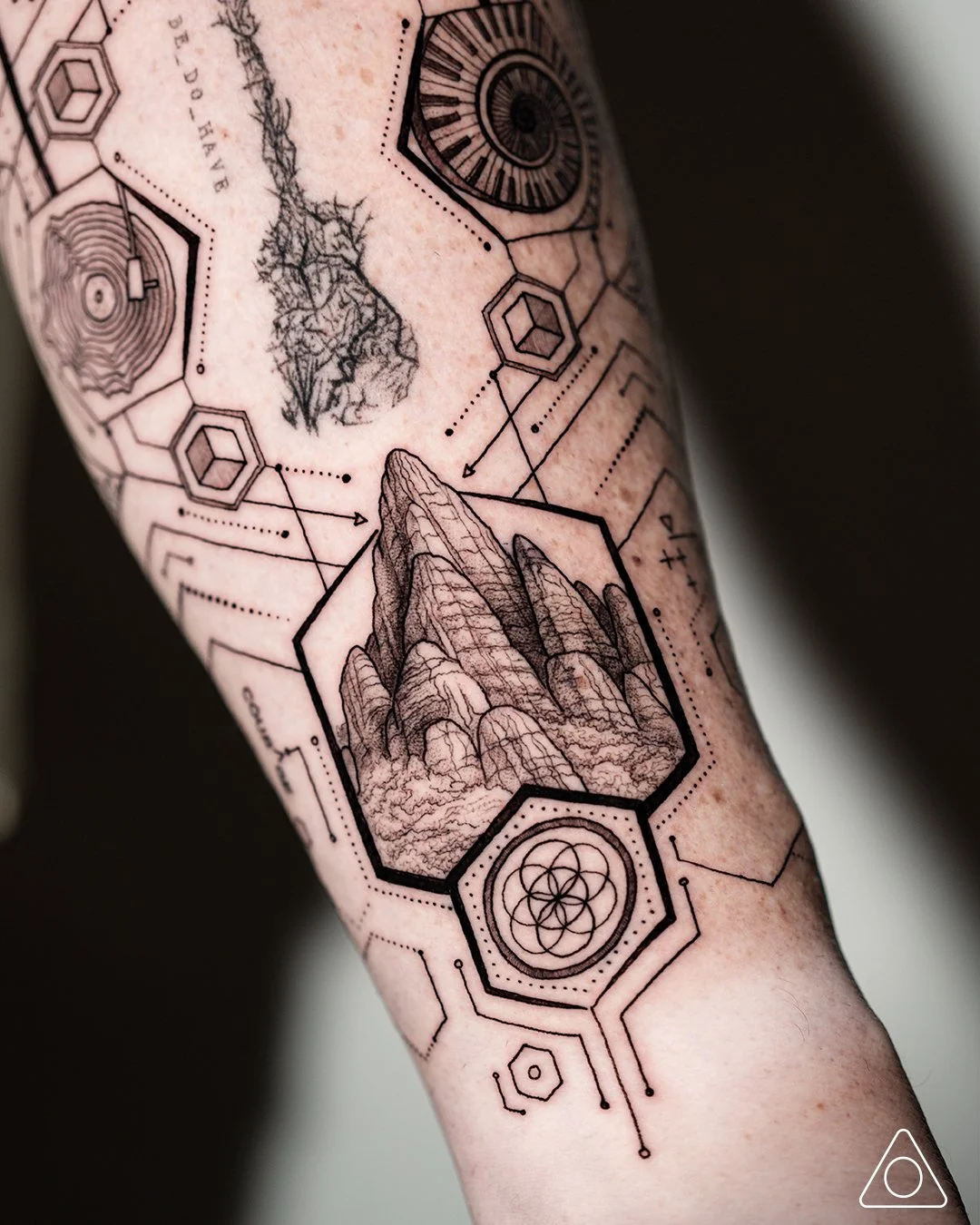 Close-up of fine-line geometric forearm tattoo showing a red rock mountain peak above sacred geometry, symbolizing courage and life’s ascent, created by tattoo artist in Dallas, Texas